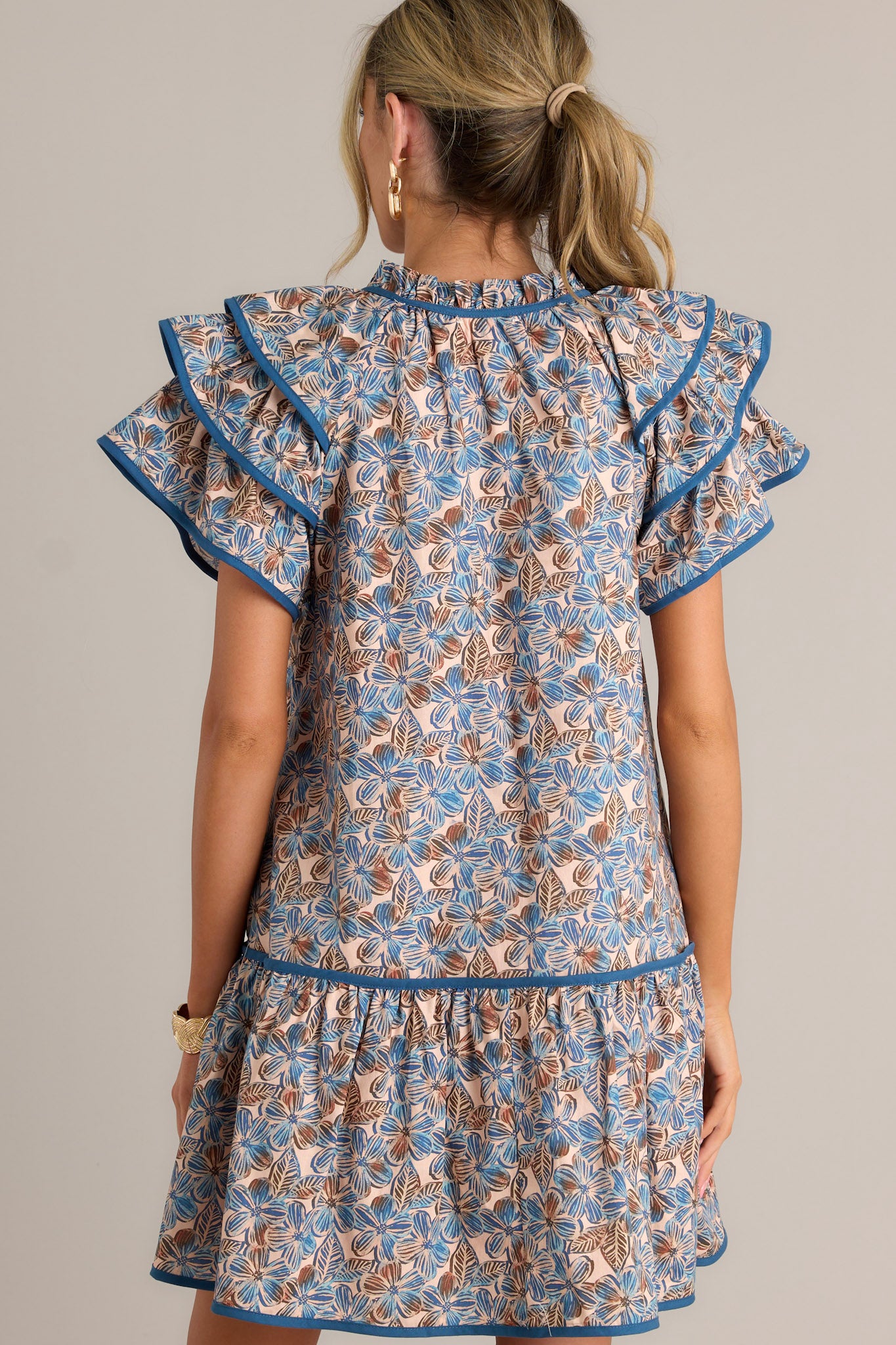 Back view of a blue floral mini dress highlighting the relaxed fit, single tier, and overall design.