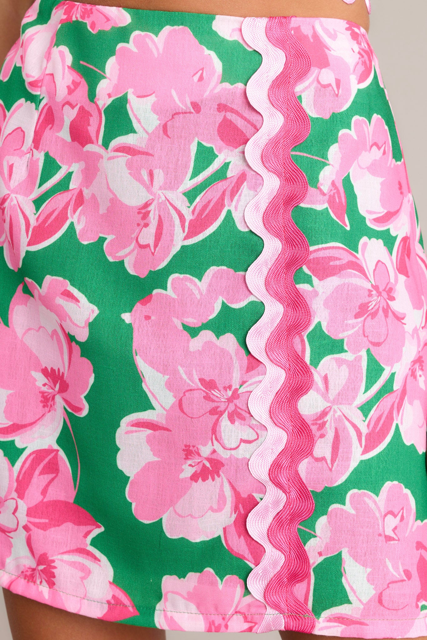 Close-up of the green floral mini skirt showing the functional zipper, ricrac detailing, and floral print.