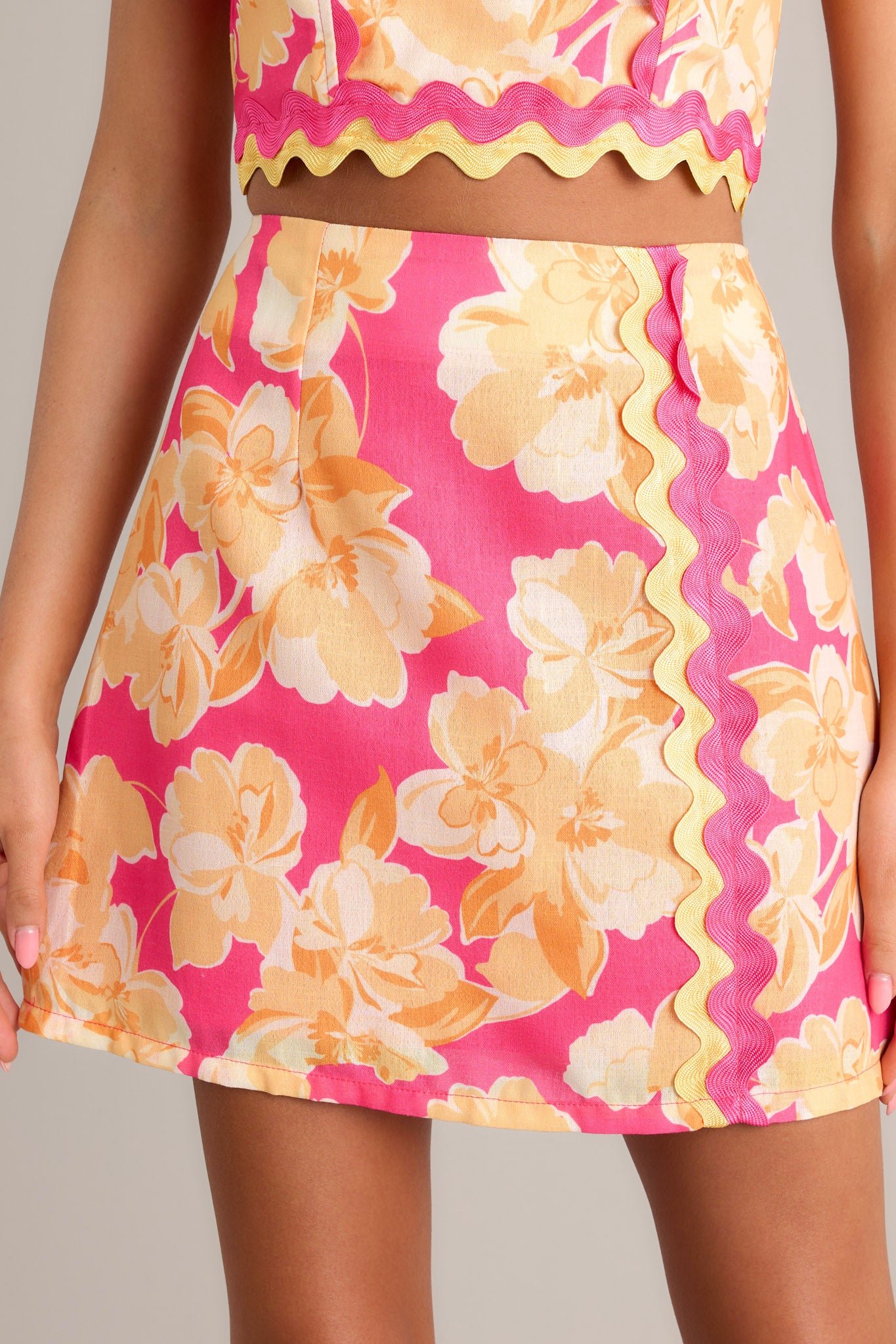 Close-up of the pink floral mini skirt showing the functional zipper, ricrac detailing, and floral print.