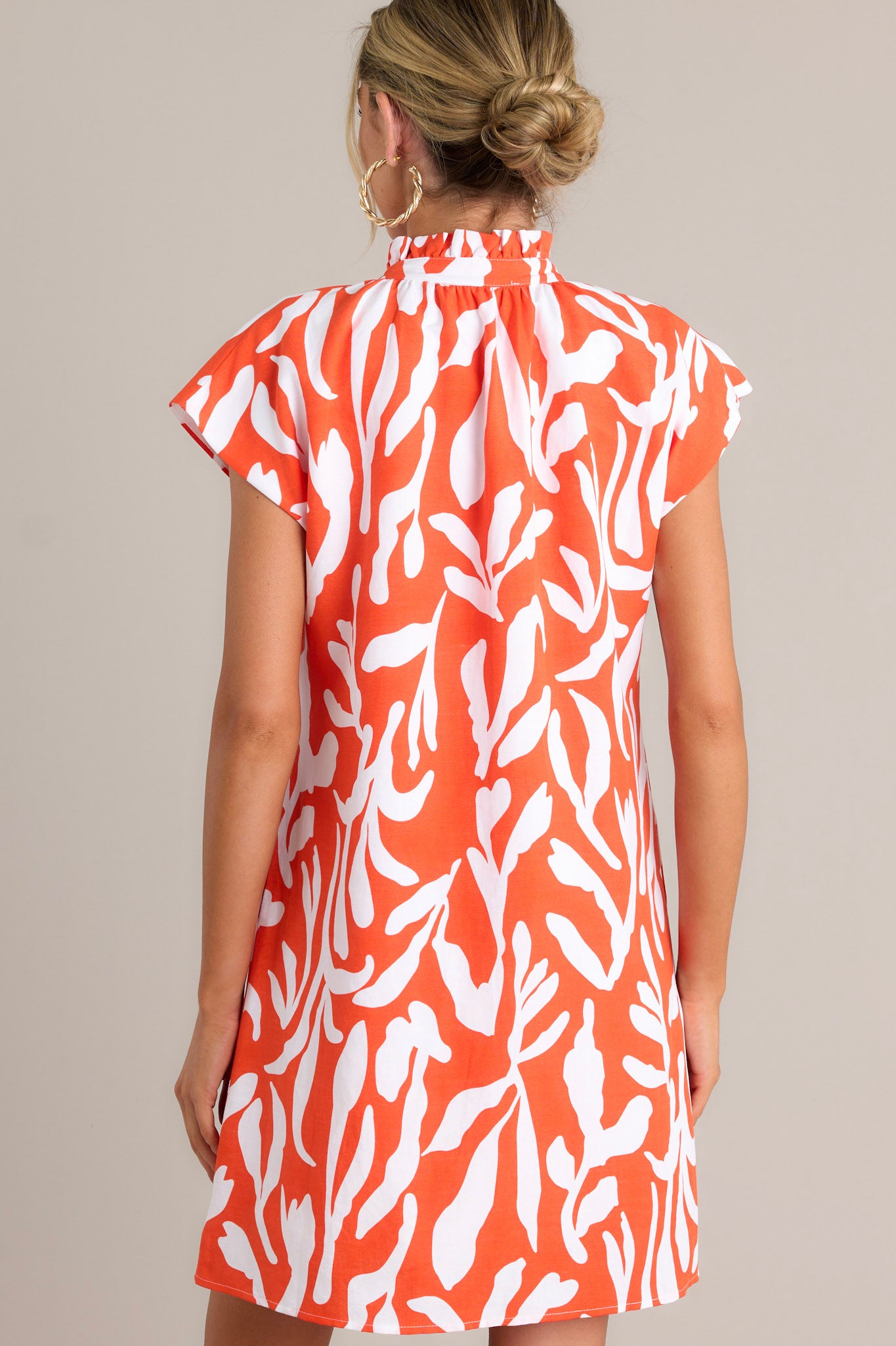 Back view of a red orange dress highlighting the caped short sleeves, fun abstract print, and overall fit.