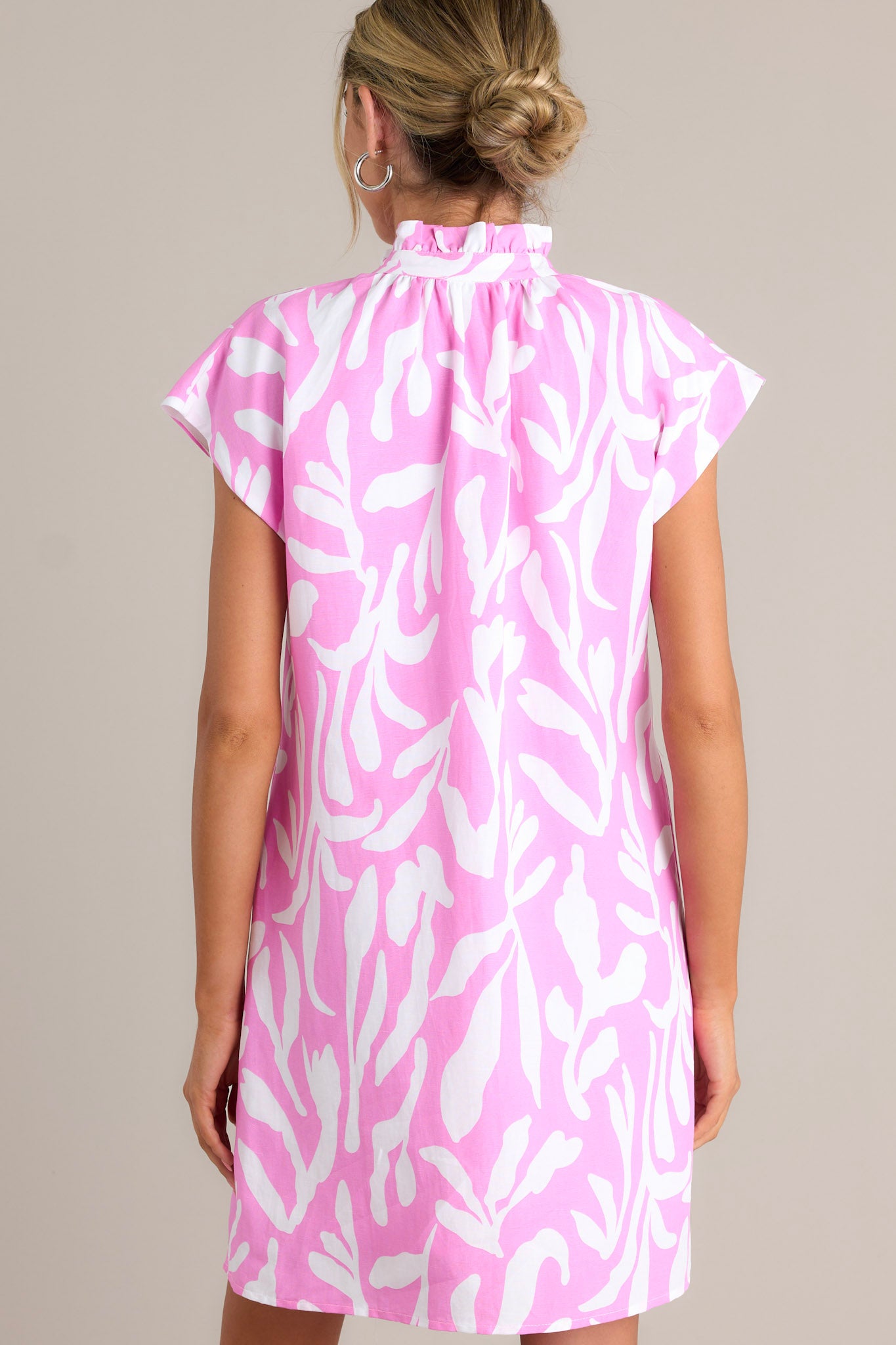 Back view of a pink dress highlighting the ruffled collar, caped short sleeves, and overall fit.