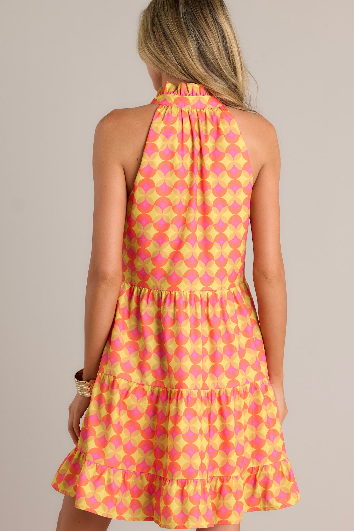 Back view of an orange mini dress highlighting the unique pattern, multiple tiers, and overall fit.