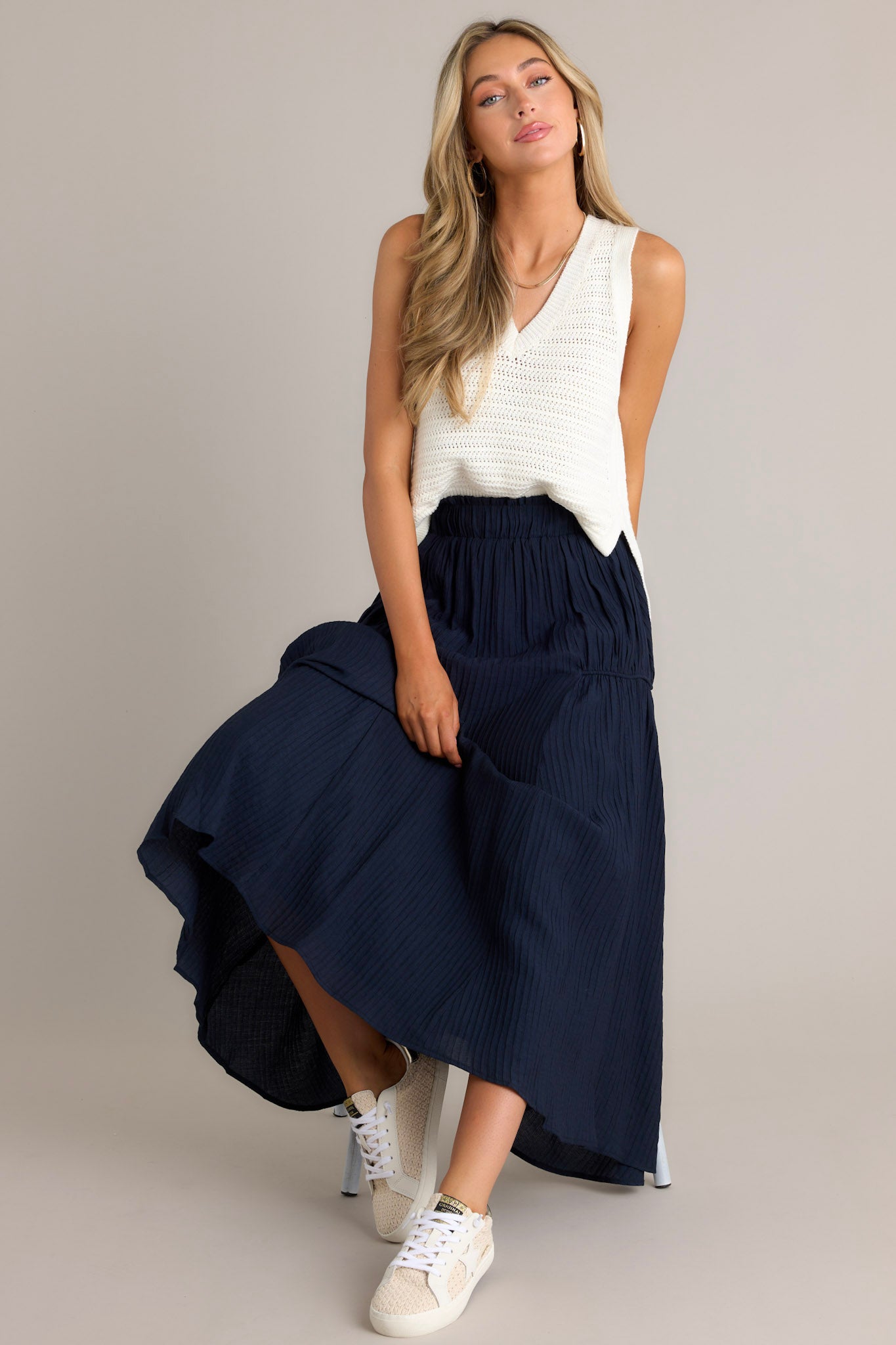 Seated Full length view of a navy skirt with a high waist design, an elastic waistband, a ribbed texture, and a flowing silhouette