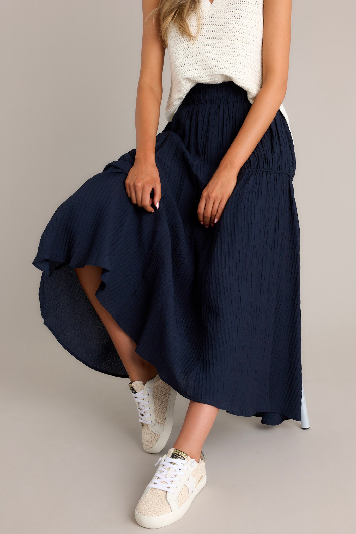 Seated Front view of a navy skirt featuring a high waist design, an elastic waistband, a ribbed texture, and a flowing silhouette.