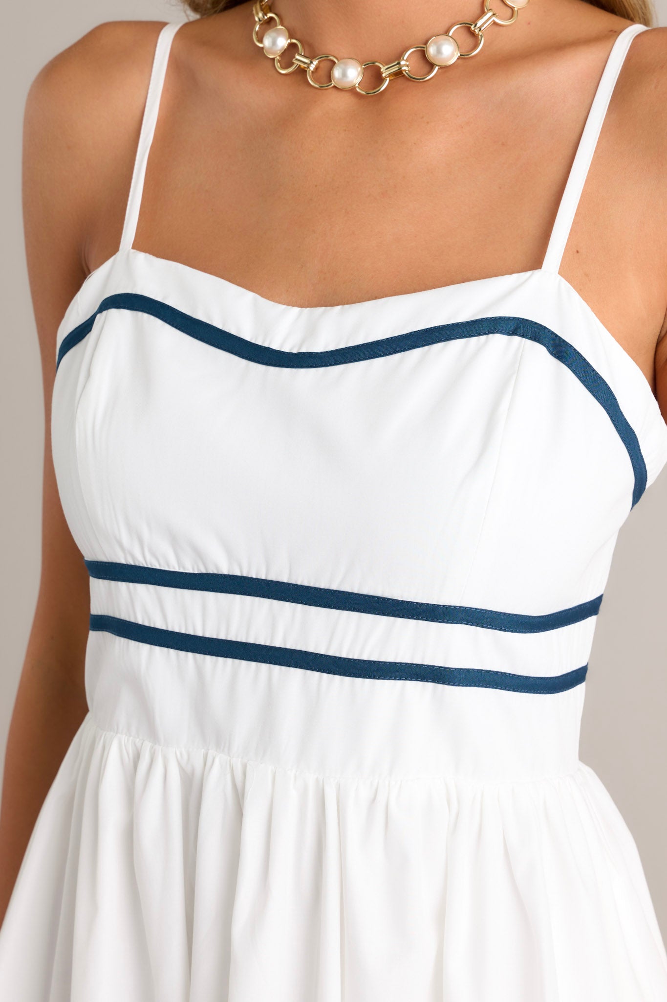 Close-up of the ivory midi dress showing the slight sweetheart neckline, navy trim, and the navy striped waist.