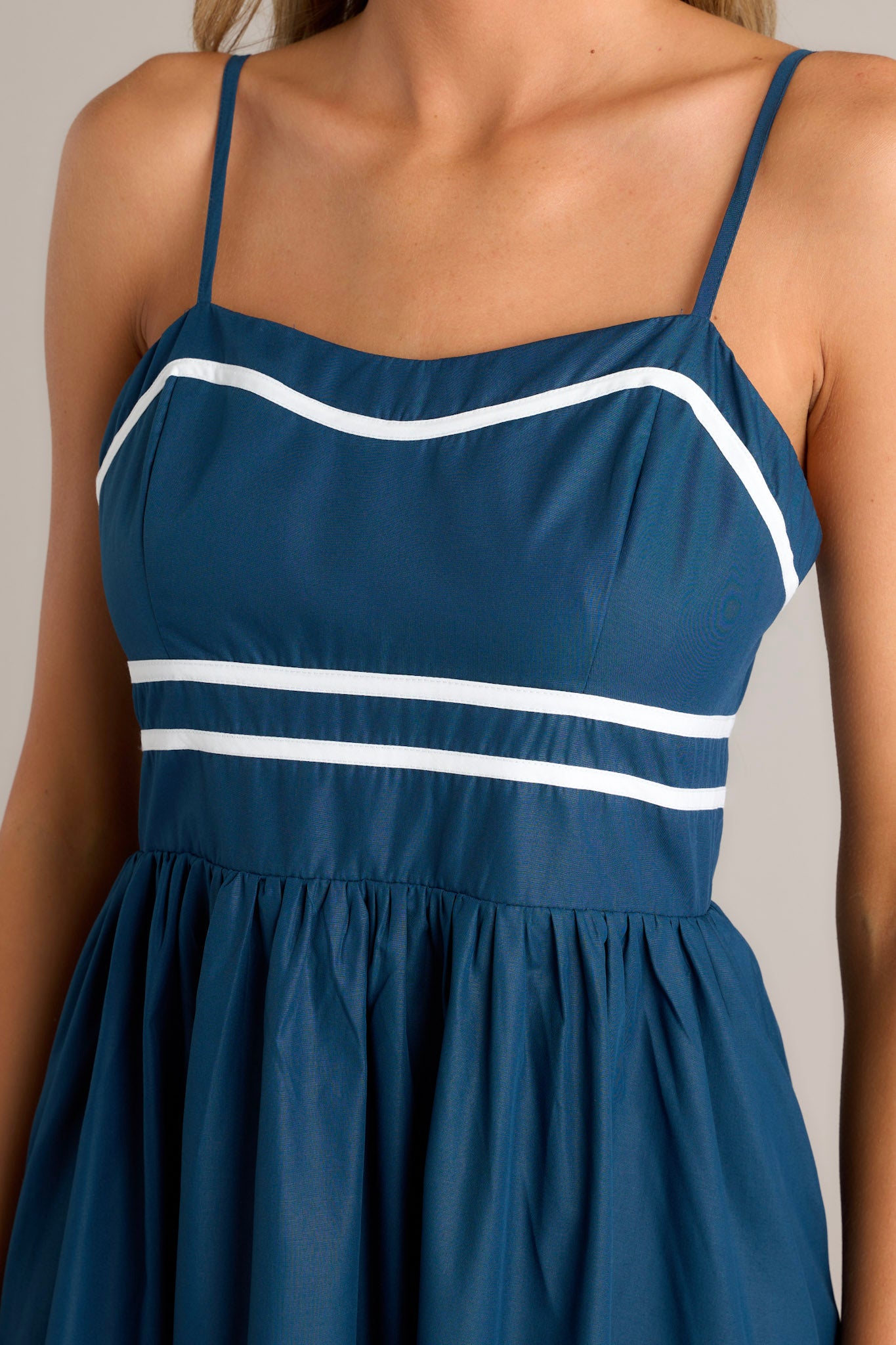 Close-up of the navy midi dress showing the slight sweetheart neckline, ivory trim, and ivory striped waist.