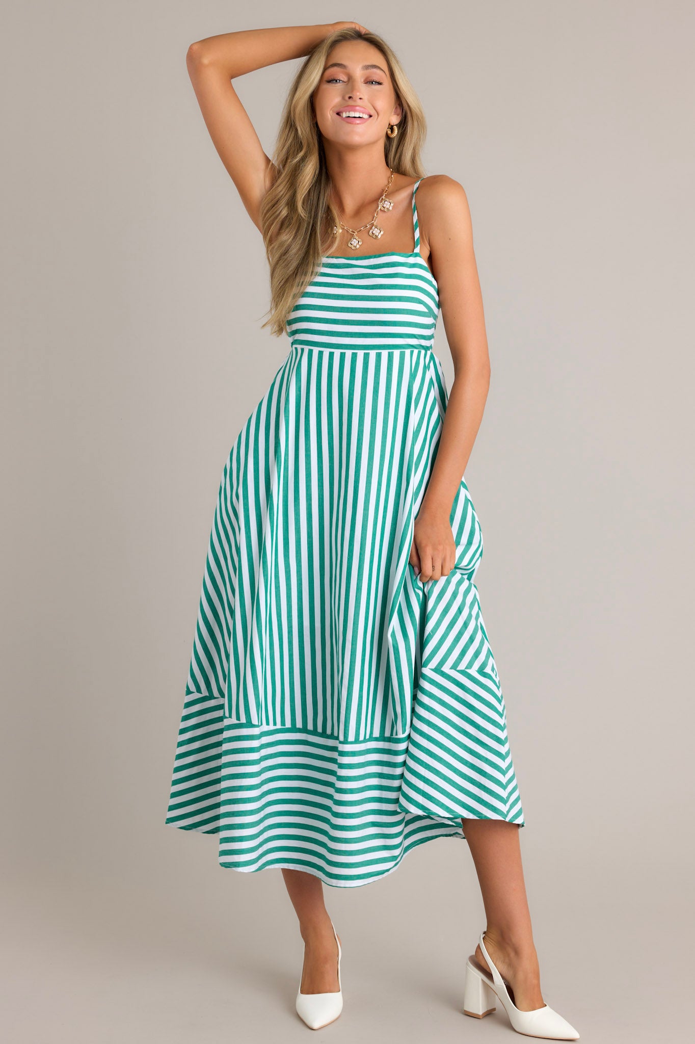 Full length view of a green stripe midi dress with a square neckline, thin adjustable straps, a smocked back insert, functional hip pockets, and horizontal & vertical stripes