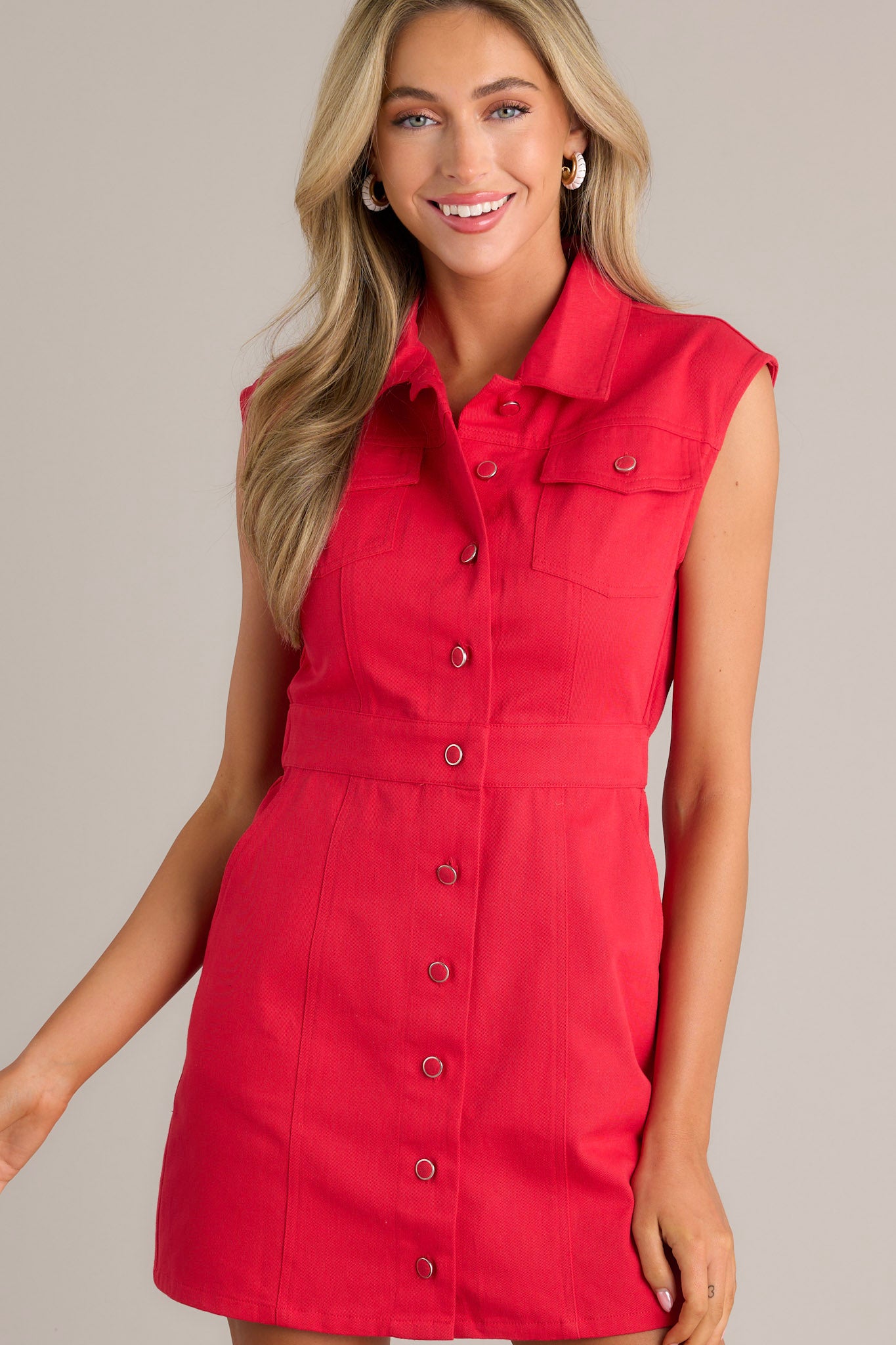 Front view of a red mini dress featuring a collared neckline, a full button front, functional breast pockets, an elastic insert in the back of the waist, functional hip pockets, and a sleeveless design.  Side