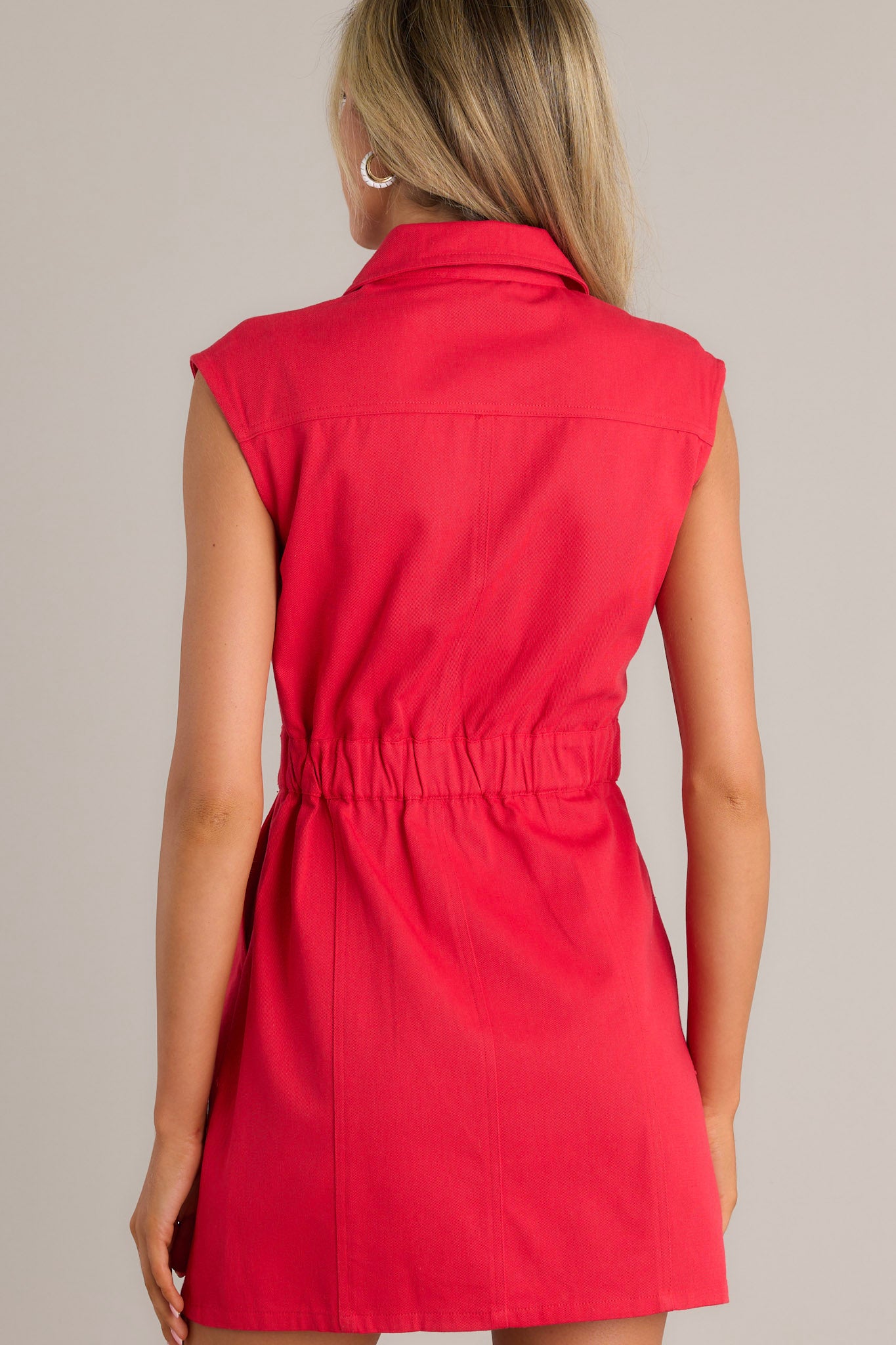 Back view of a red mini dress highlighting the collared neckline, elastic insert in the back of the waist, functional hip pockets, and the sleeveless design.