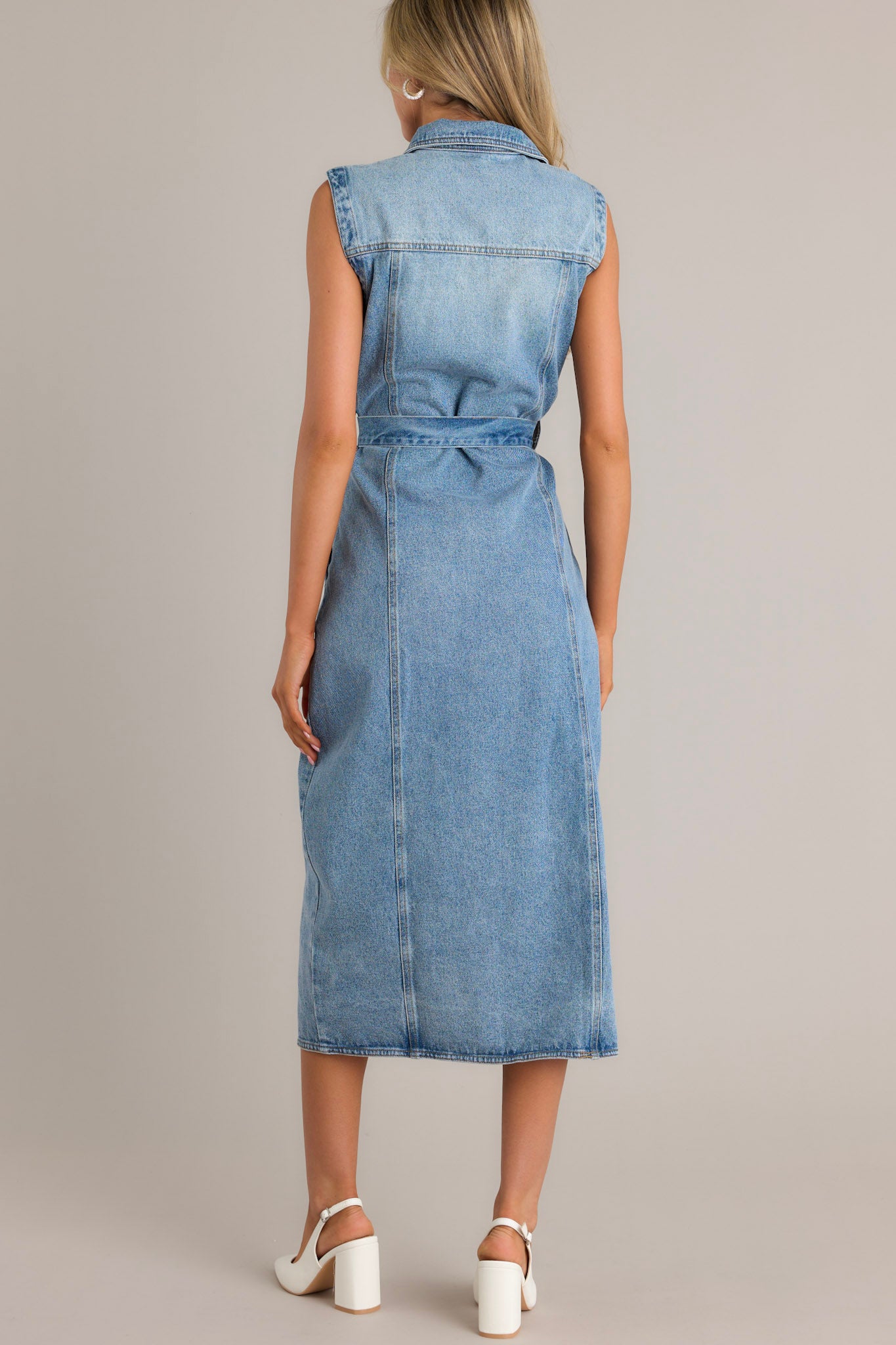 Back view of a denim maxi dress highlighting the collared neckline, self-tie waist belt, belt loops, functional hip pockets, and the sleeveless design.