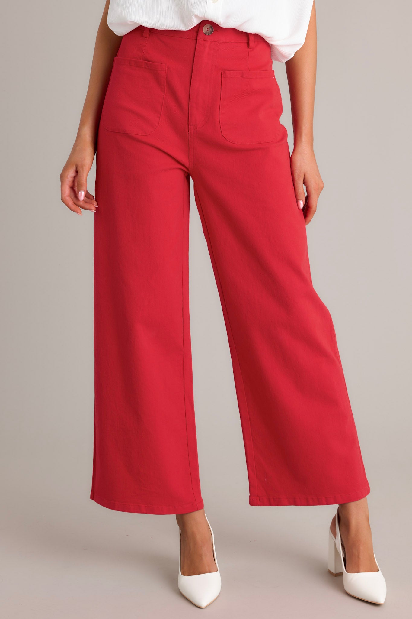 Front view of red pants featuring a high waisted design, classic button & zipper closure, belt loops, functional front pockets, faux back pockets, and a wide leg design.