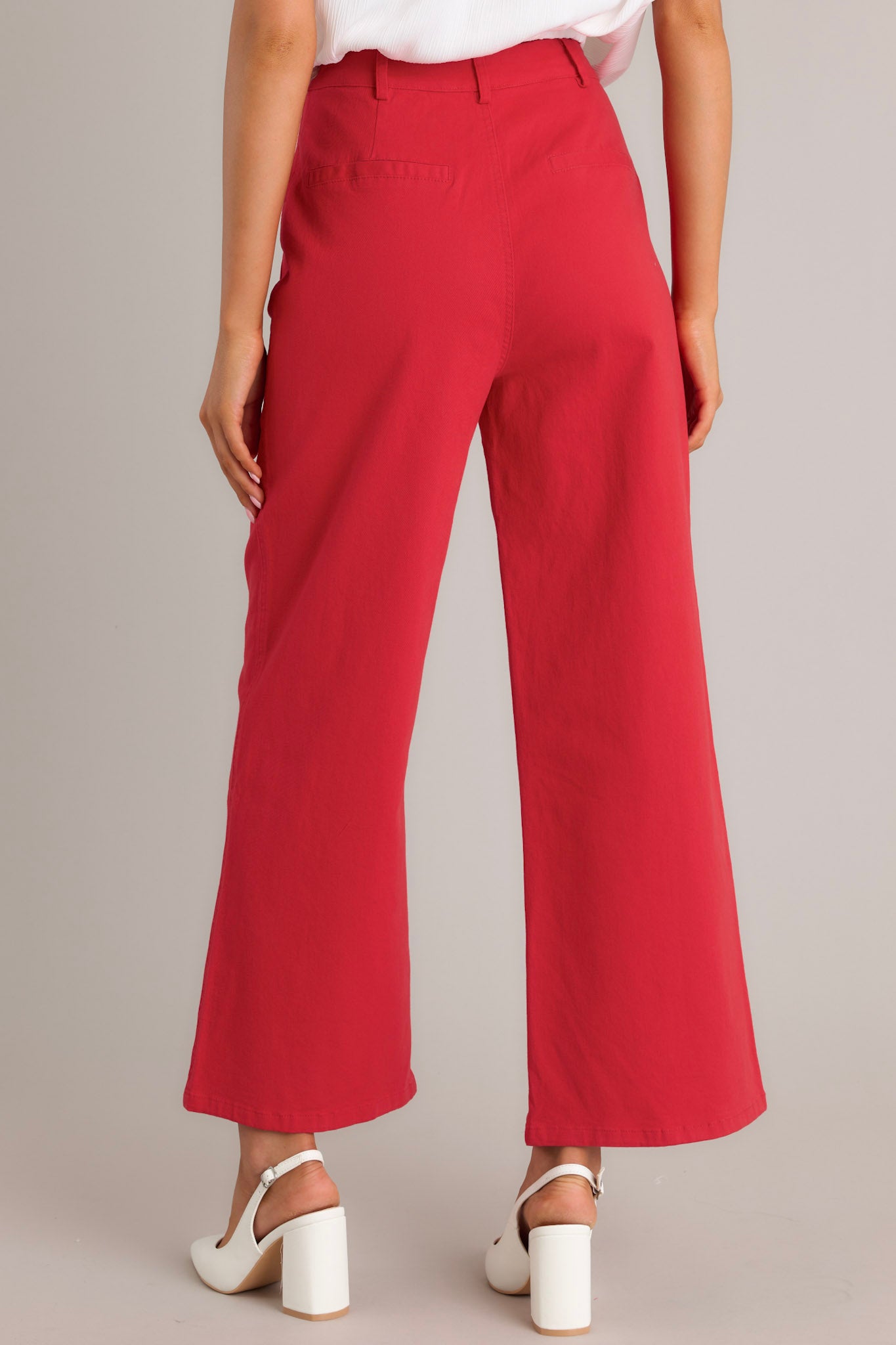 Back view of red pants highlighting the high waisted design, belt loops, faux back pockets, and the wide leg design.