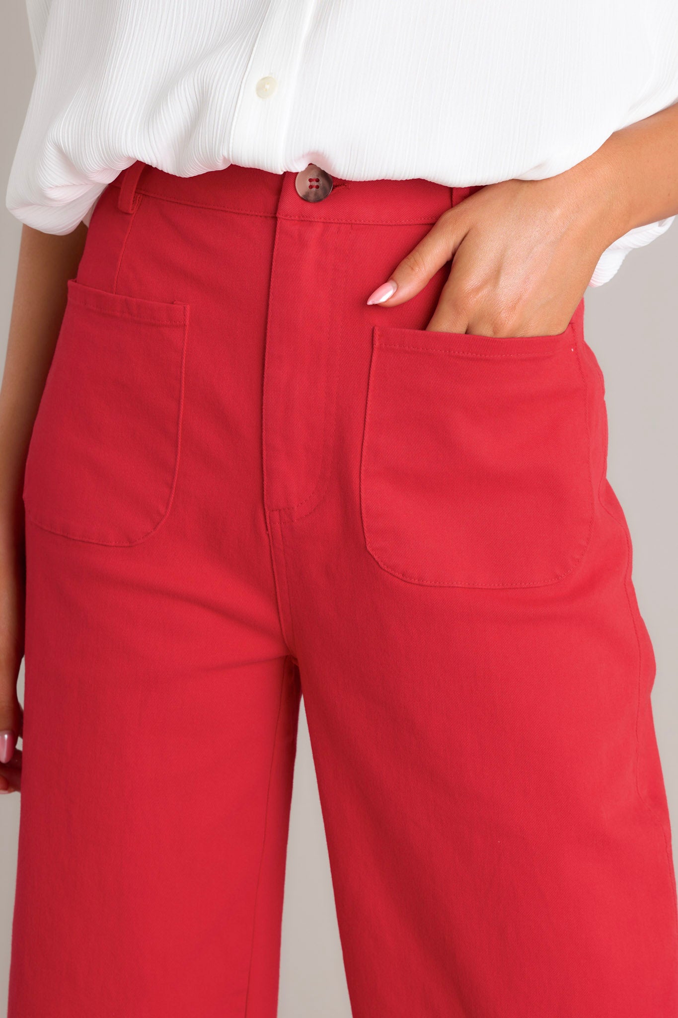 Close-up of the red pants showing the high waisted design, classic button & zipper closure, belt loops, and functional front pockets.