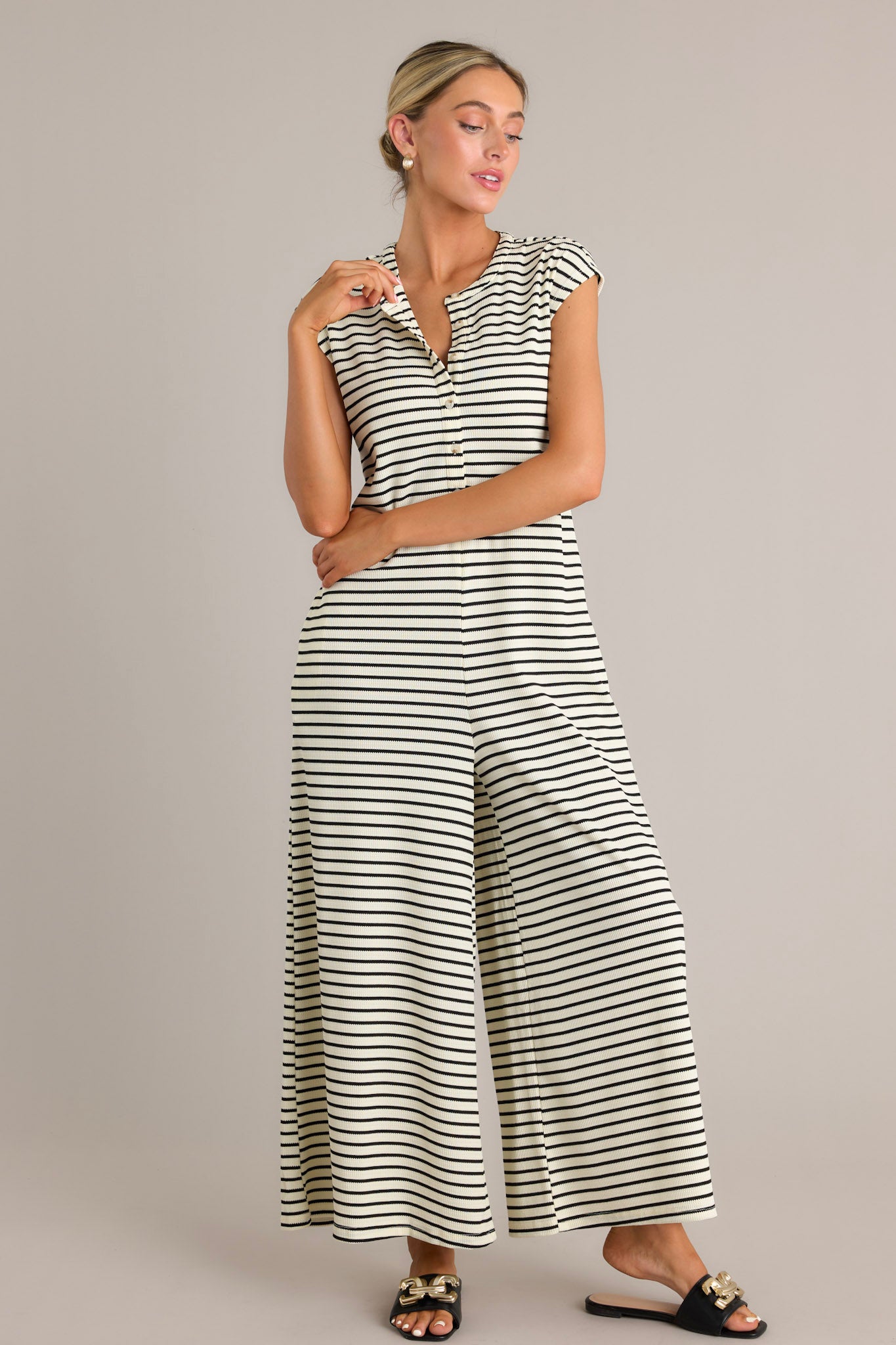 Front angled view of a black striped jumpsuit featuring a rounded neckline, functional button front bodice, functional hip pockets, a textured material, and a sleeveless design