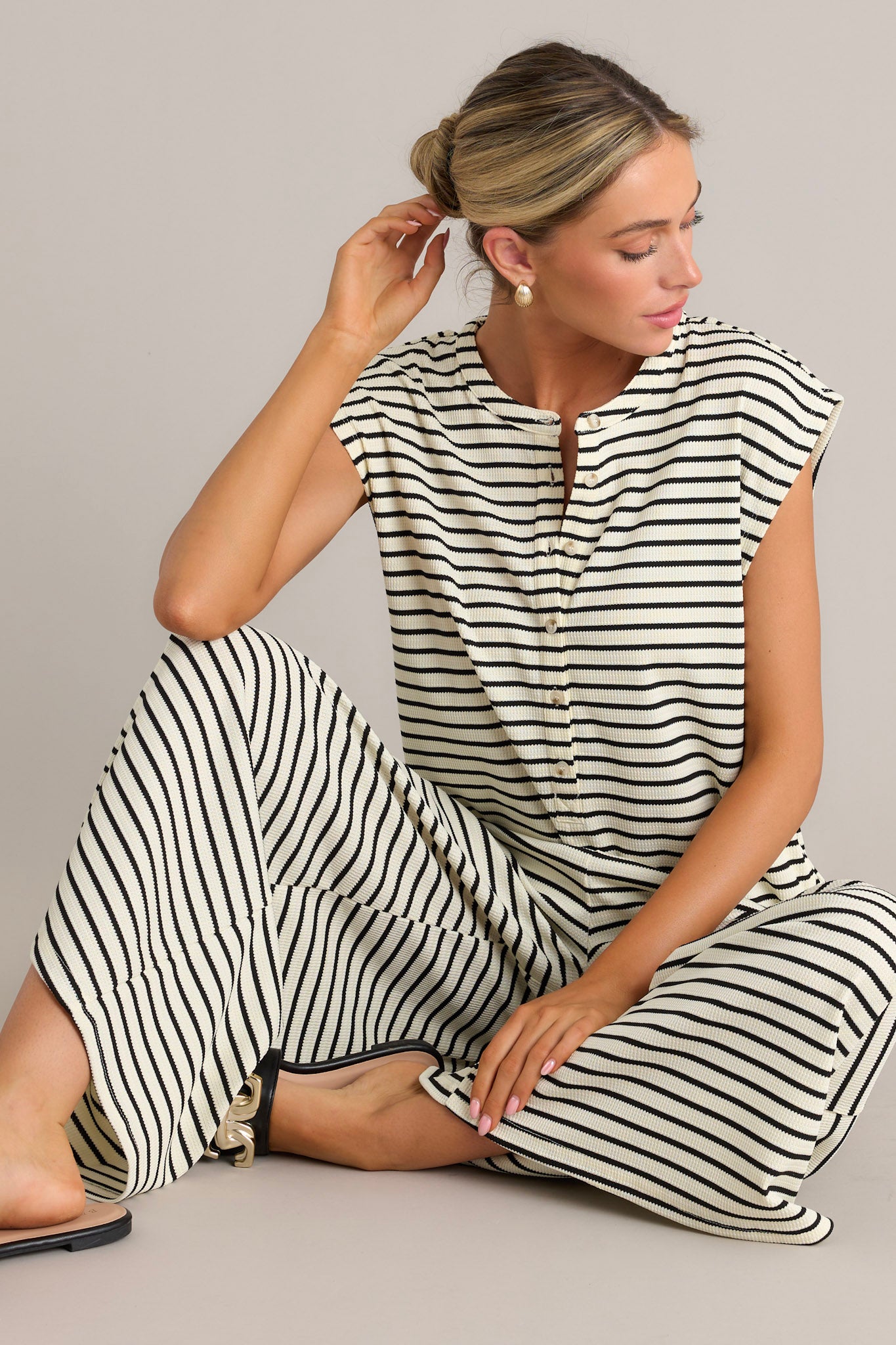 This black striped jumpsuit features a rounded neckline, functional button front bodice, functional hip pockets, a textured material, and a sleeveless design.