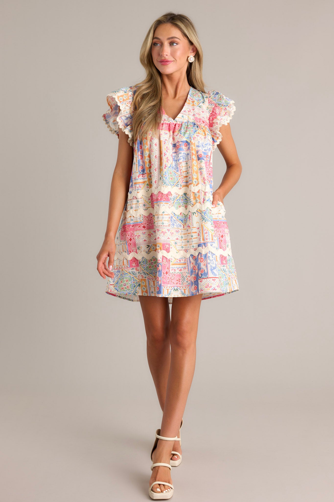 Full length view of a patchwork mini dress with a v-neckline, unique patchwork design, functional hip pockets, ricrac detailing, and ricrac trim flutter sleeves