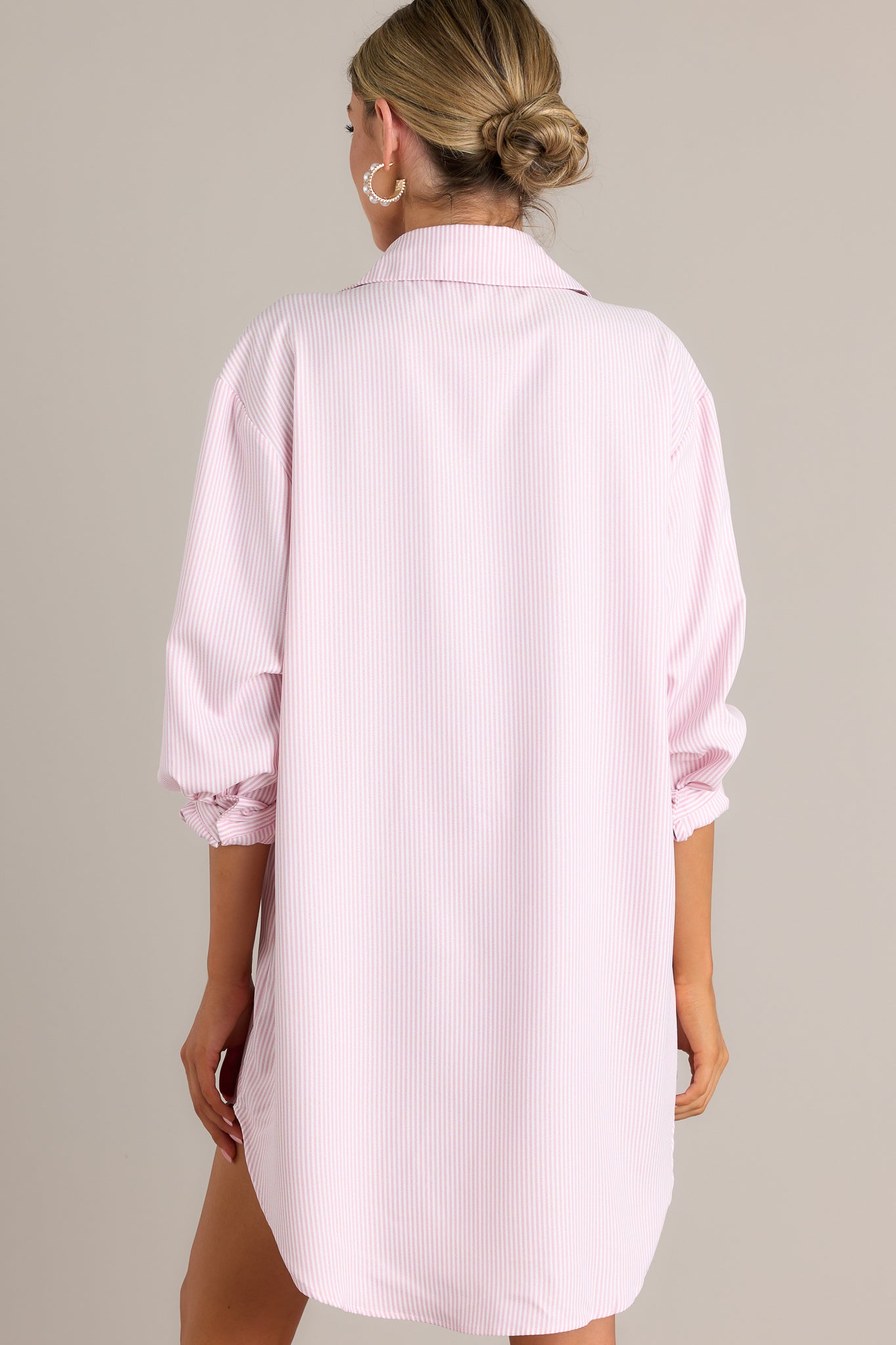 Back view of a pink stripe shirt dress highlighting the overall fit, long sleeves with buttoned cuffs, and scoop bottom hem.