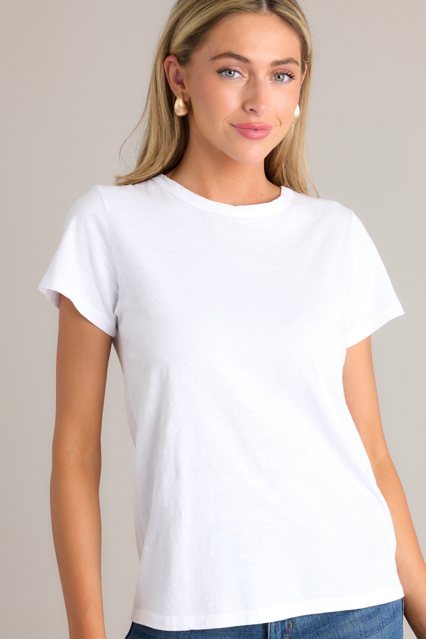 This white top features a high crew neckline, lightweight material, an intentional exposed seam in the back, and short sleeves. 