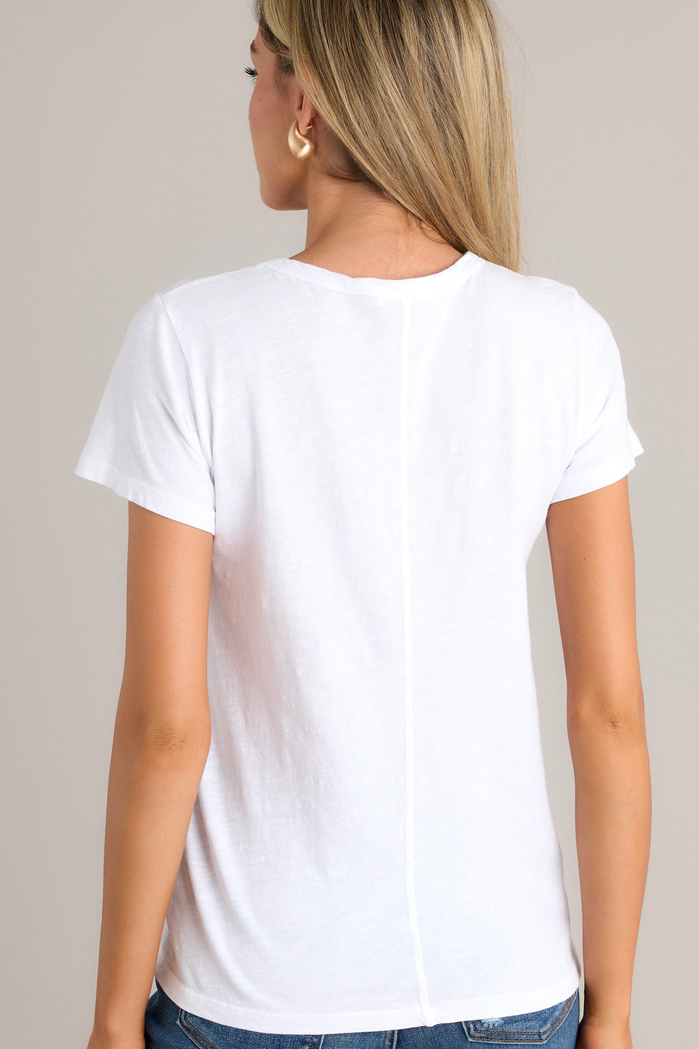 Back view of  this top that features a high crew neckline, lightweight material, an intentional exposed seam in the back, and short sleeves.