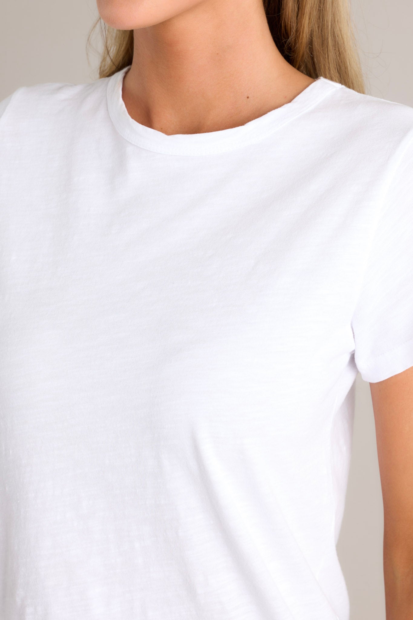 Close up view of this top that features a high crew neckline, lightweight material, an intentional exposed seam in the back, and short sleeves. 