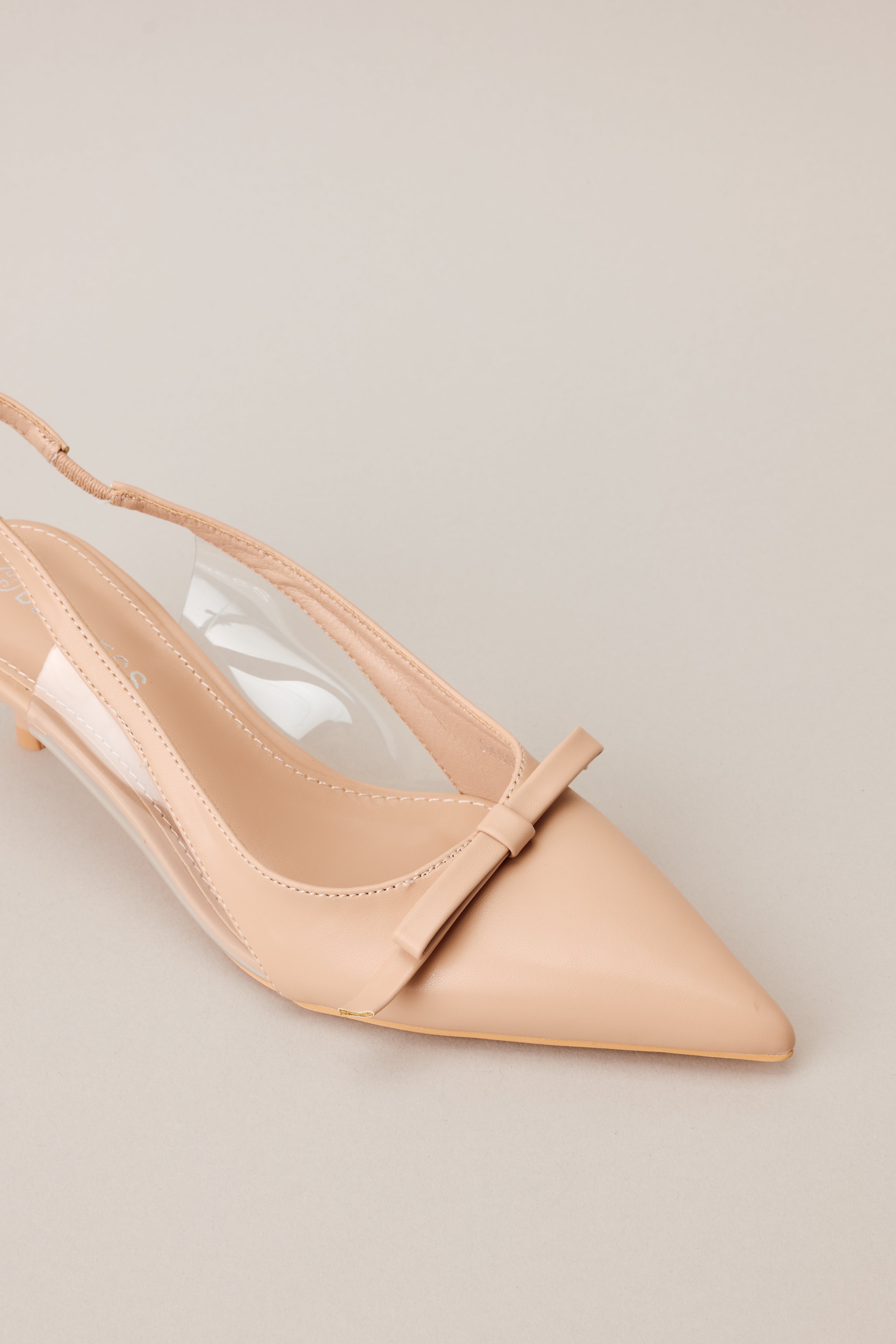 Close-up of the beige kitten heels showing the pointed closed toe, delicate bow detailing, and clear siding for extra support.