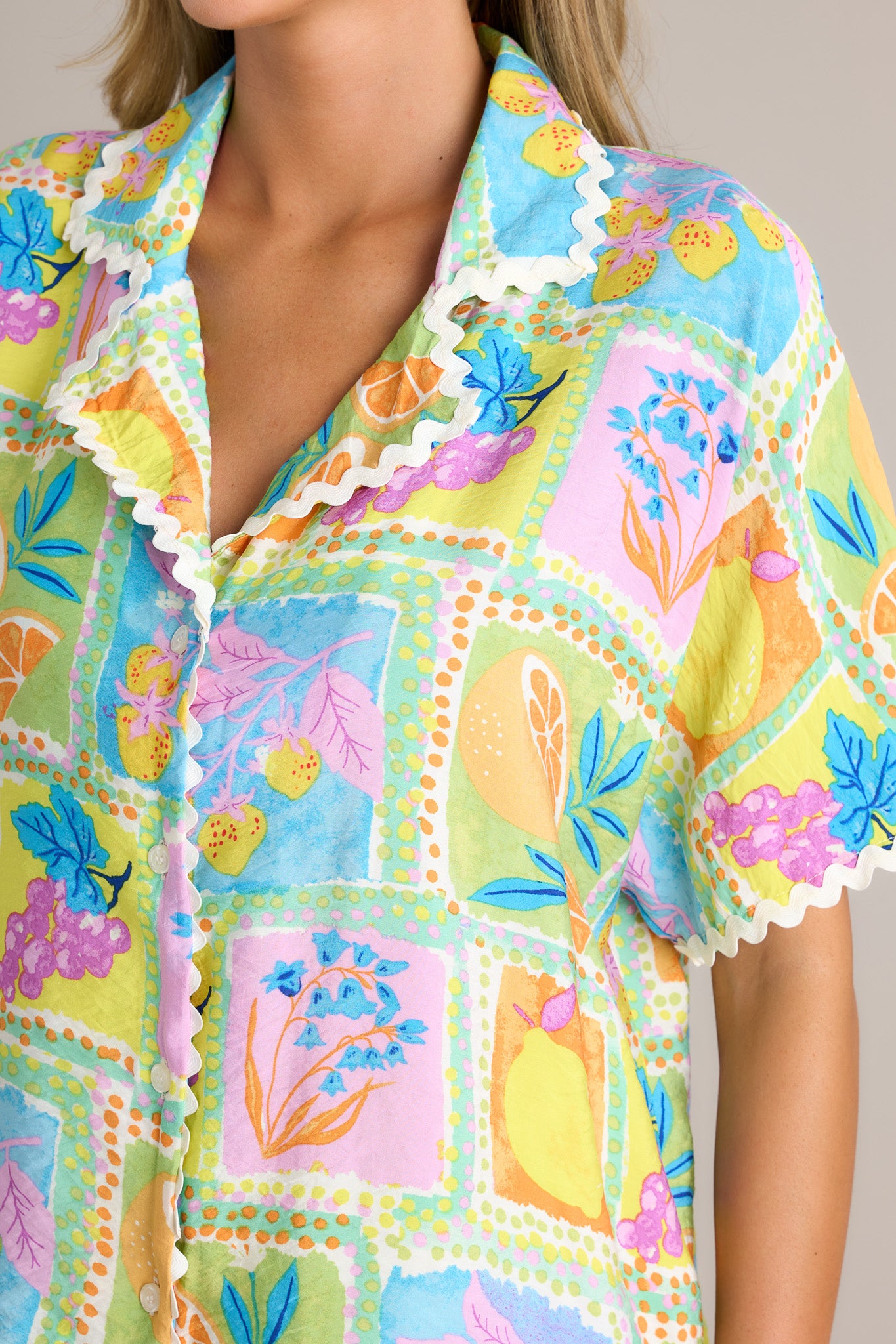 Close-up of the tropical ricrac top showing the notched lapel collared neckline, functional button front, unique print, and contrasting ricrac trim.