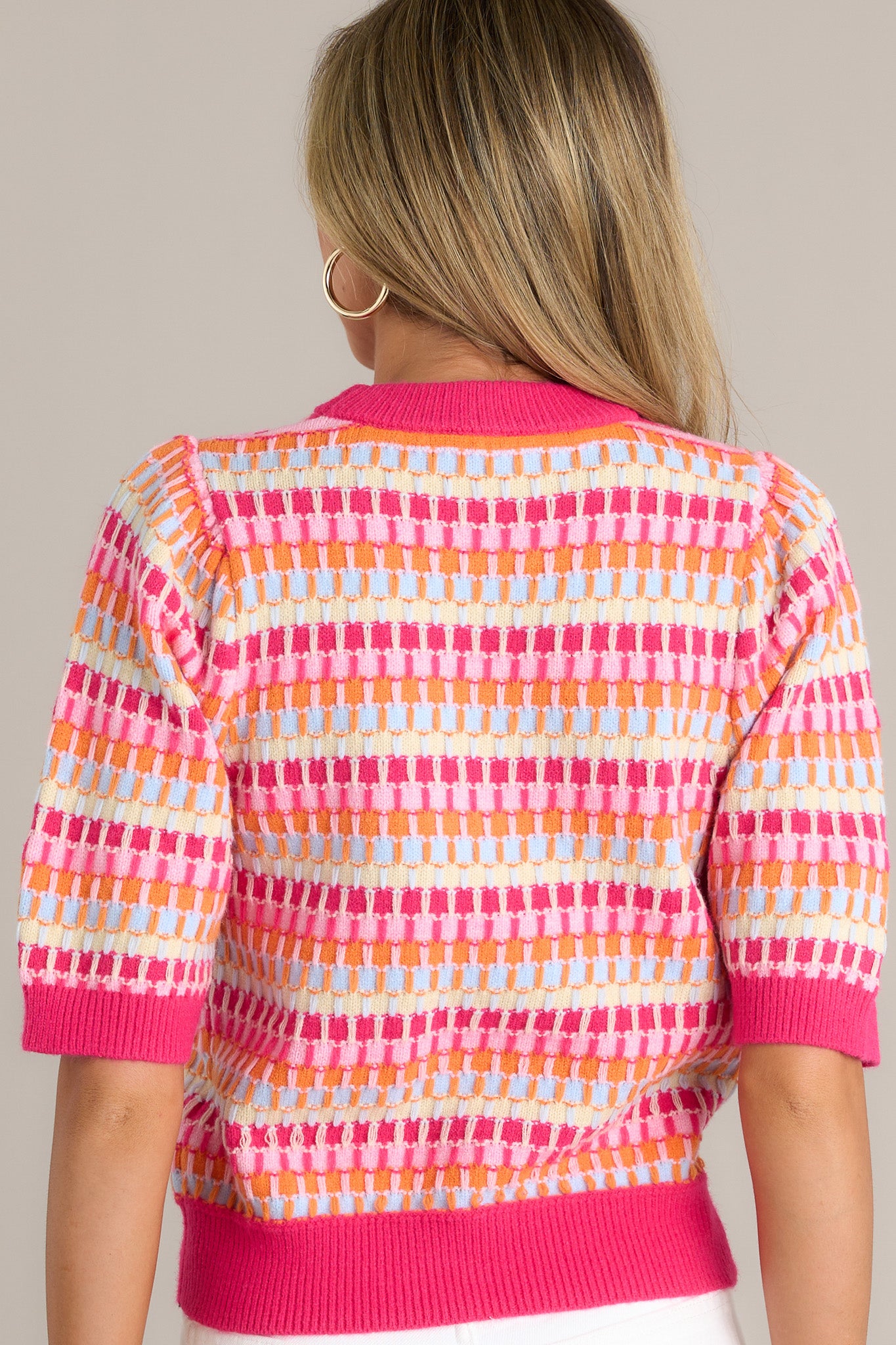 Back view of a pink stripe sweater highlighting the multicolored knitted stripes, ribbed hemline, and overall fit.