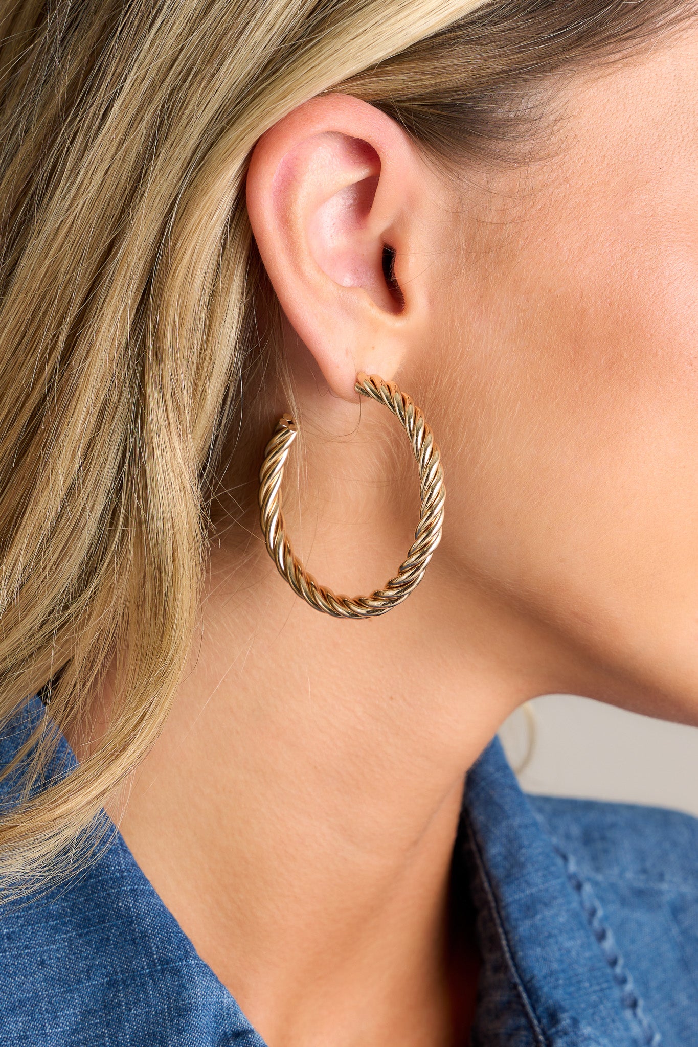 Close up view of these earrings featuring a twist c-shaped hoop design, a classic gold finish, and a secure post-back closure.