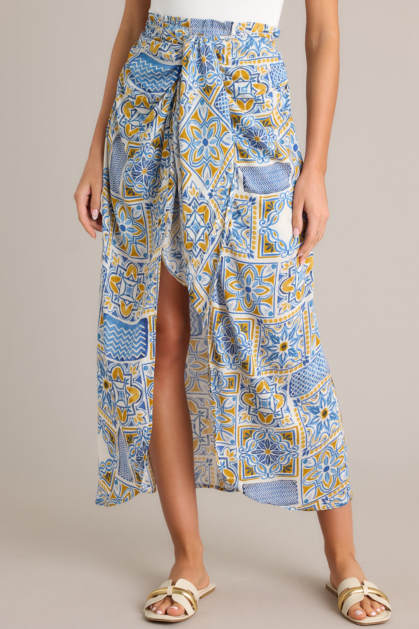 Front view of a blue maxi skirt featuring a high waisted design, an elastic waistband, a self-tie knot, an open front, a short skirt underneath, and a unique print.