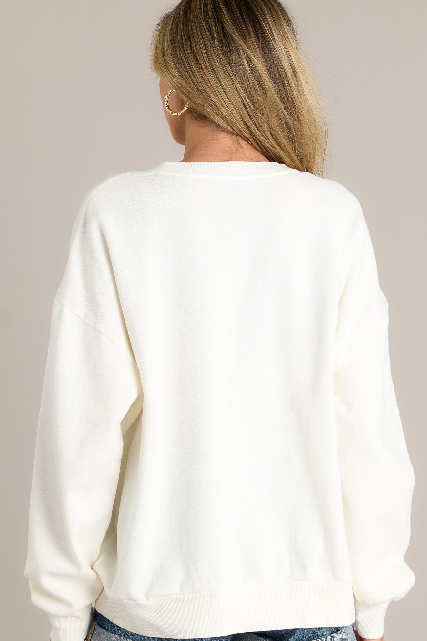 Back view of an ivory sweatshirt highlighting the overall fit, thick ribbed hemline, and ribbed cuffed long sleeves.