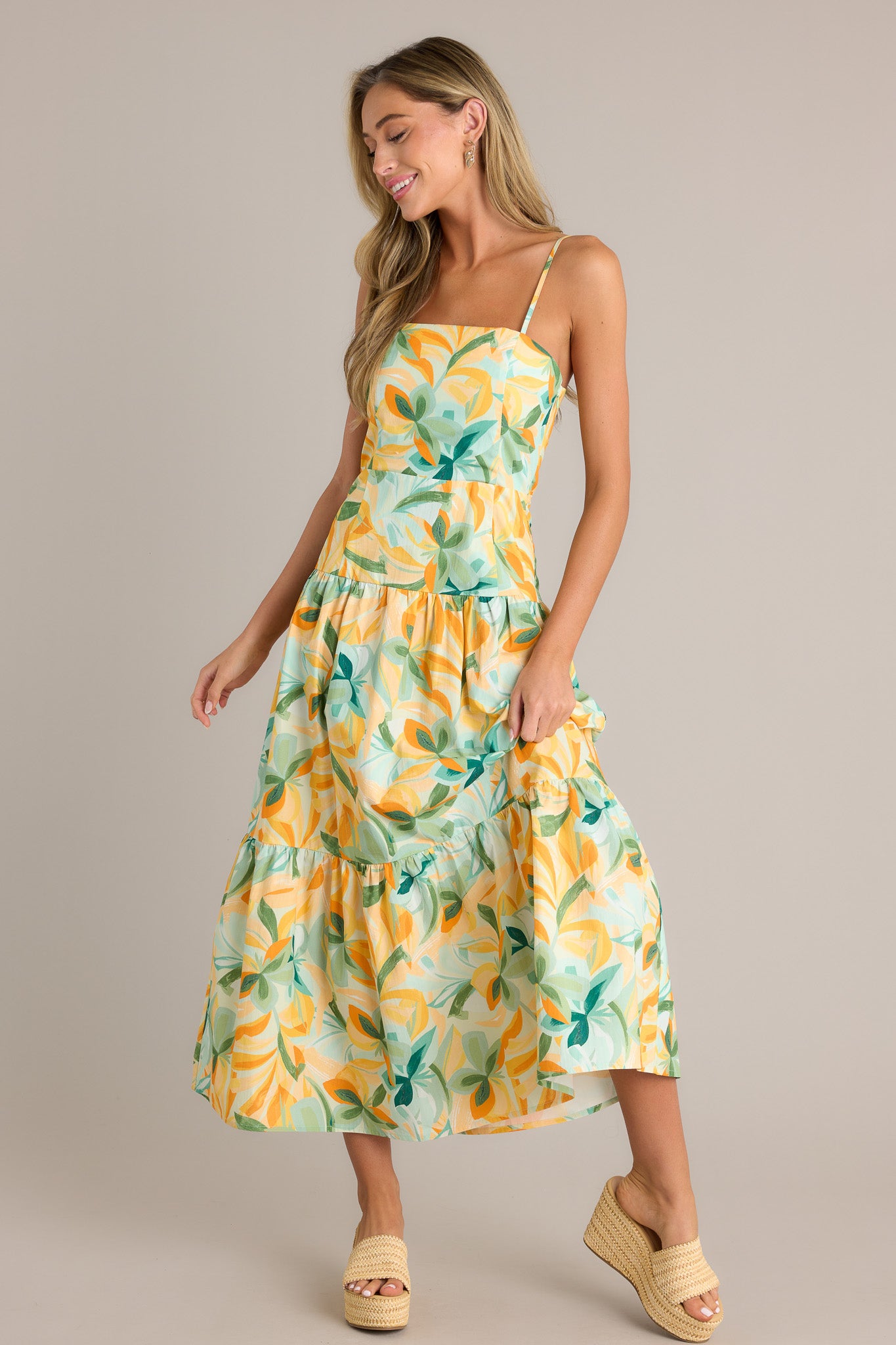 Full length view of a yellow midi dress with a square neckline, a discreet side zipper, a smocked back insert, a tiered design, and a flowing silhouette