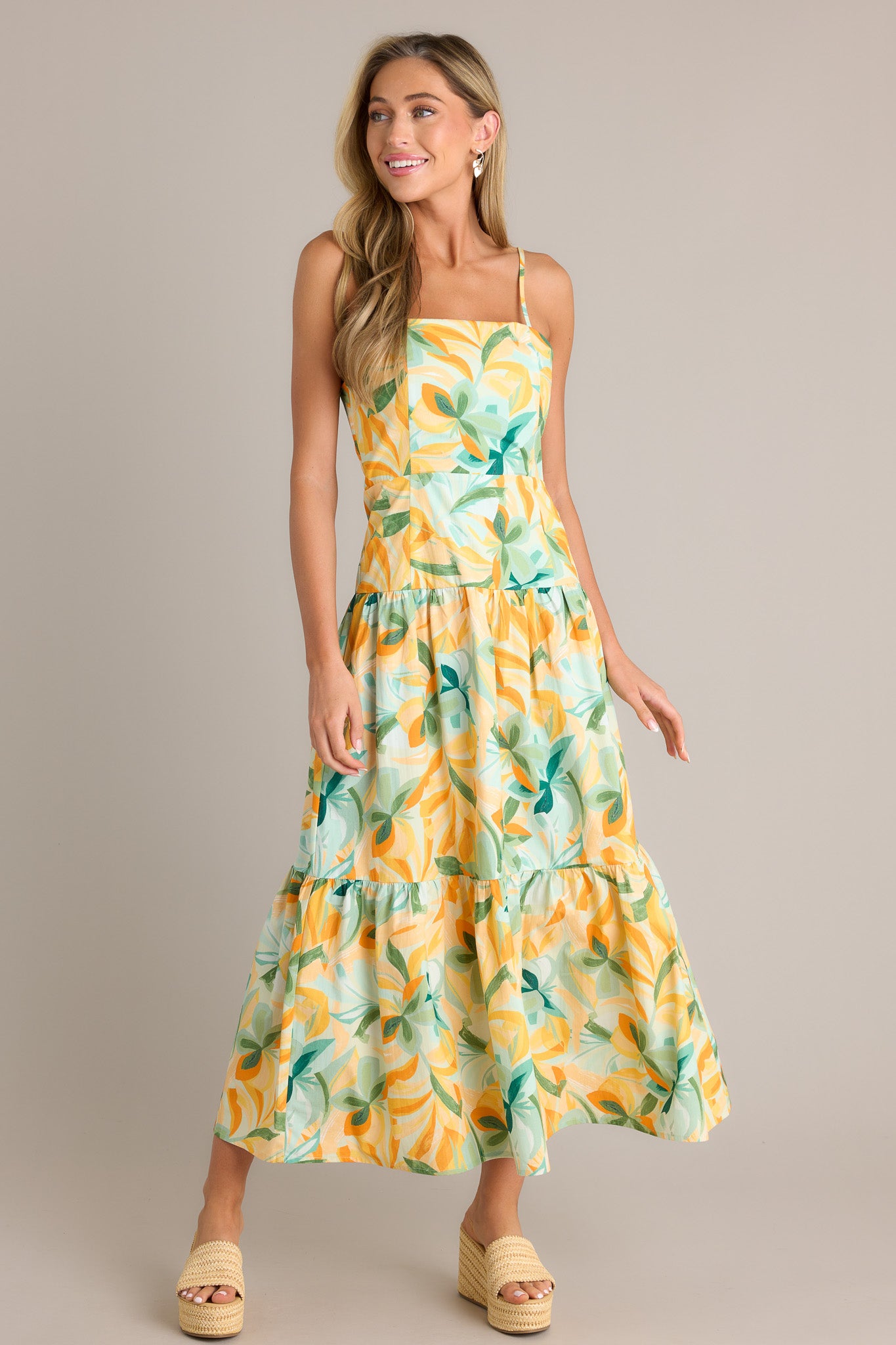 Front view of a yellow midi dress featuring a square neckline, a discreet side zipper, a smocked back insert, a tiered design, and a flowing silhouette.