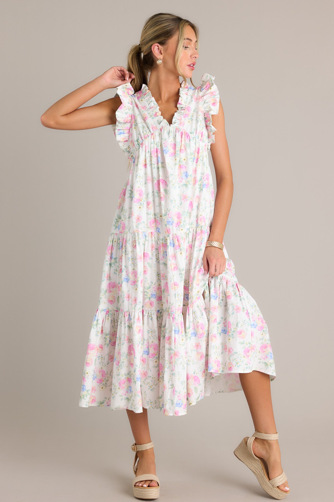 Side view of an ivory floral midi dress showcasing the ruffled v-neckline, elastic waist insert, functional hip pockets, tiers, flowing silhouette, and sleeveless design..