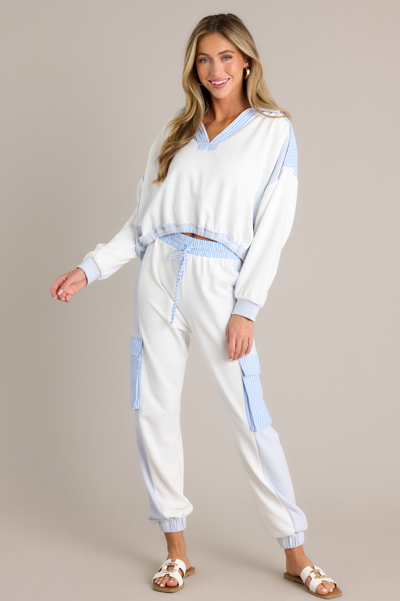 Full length view of a light blue cropped sweatshirt with a collared v-neckline, striped detailing, color blocking, an elastic waistband, an oversized fit, and cuffed long sleeves