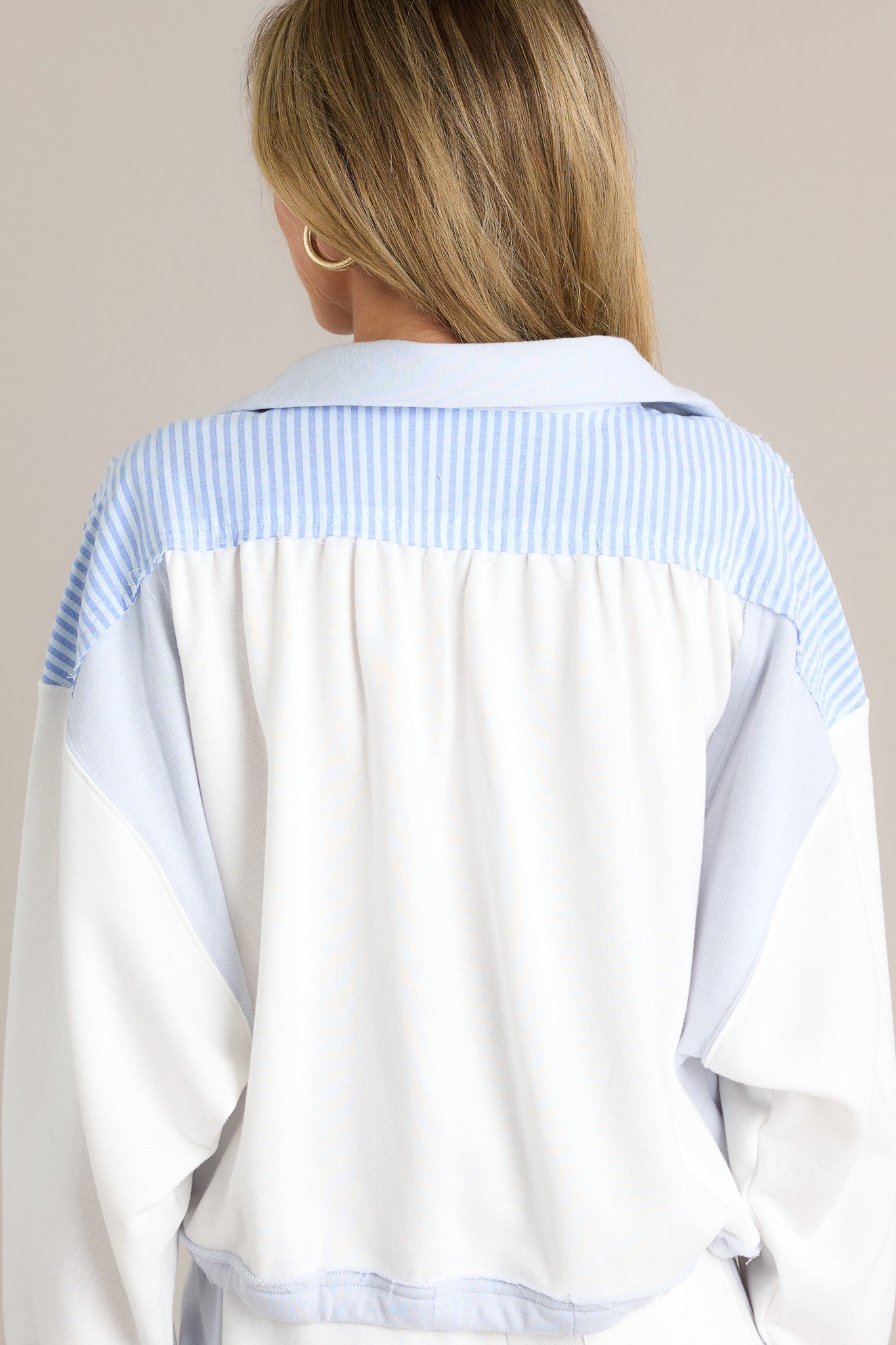 Back view of a light blue cropped sweatshirt highlighting the overall fit, color blocking, and cuffed long sleeves.