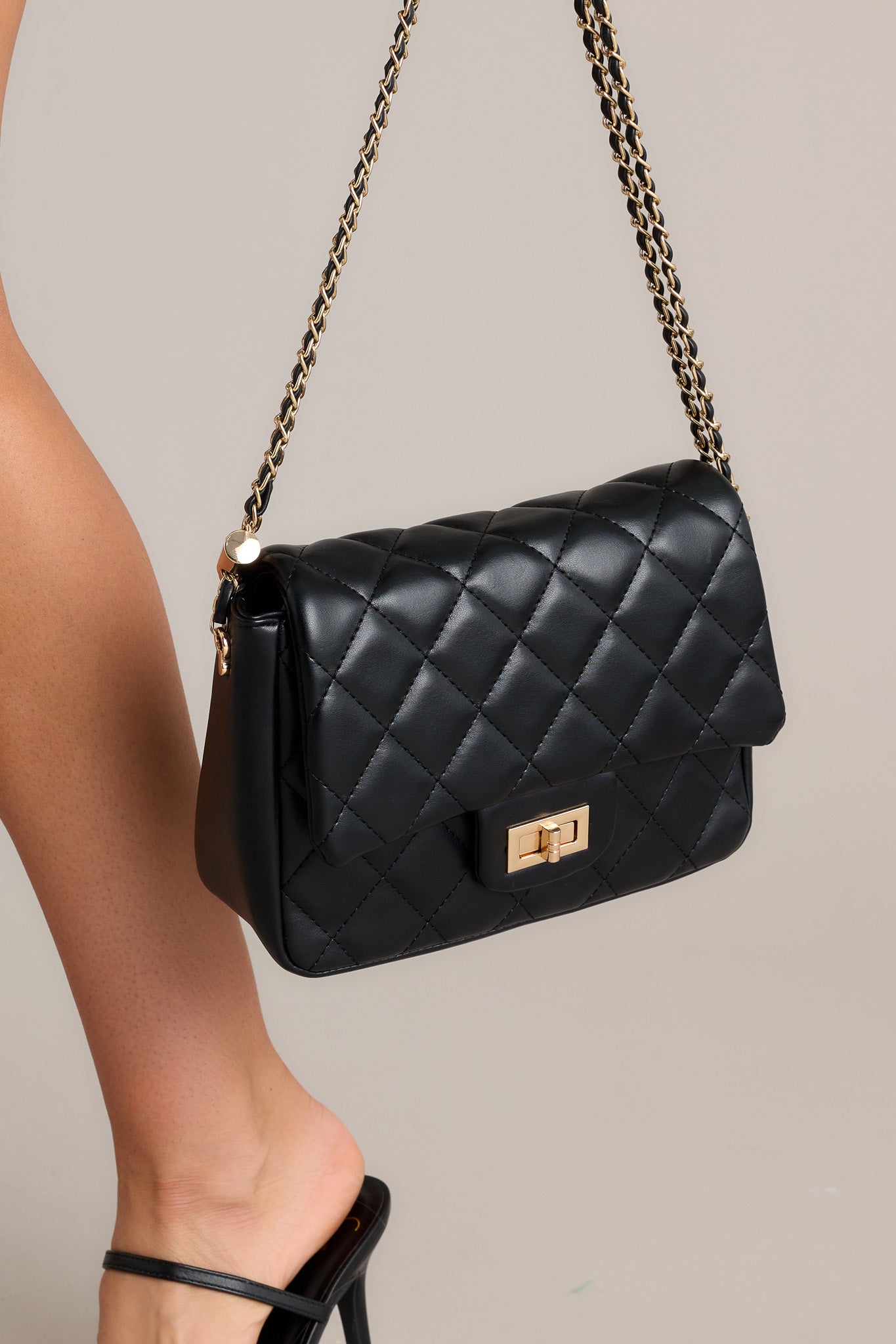 Angled side view of this black bag that features gold hardware, a quilted texture, a twist lock closure, a zipper pocket inside, and an adjustable chain strap.