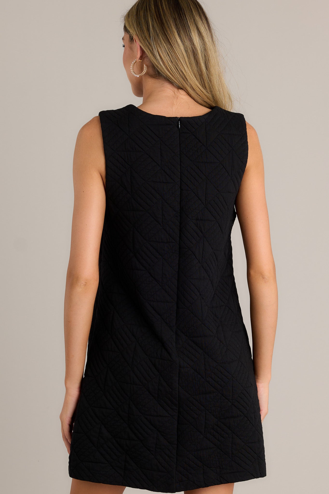 Back view of a black mini dress highlighting the overall fit, quilted fabric, and sleeveless design.