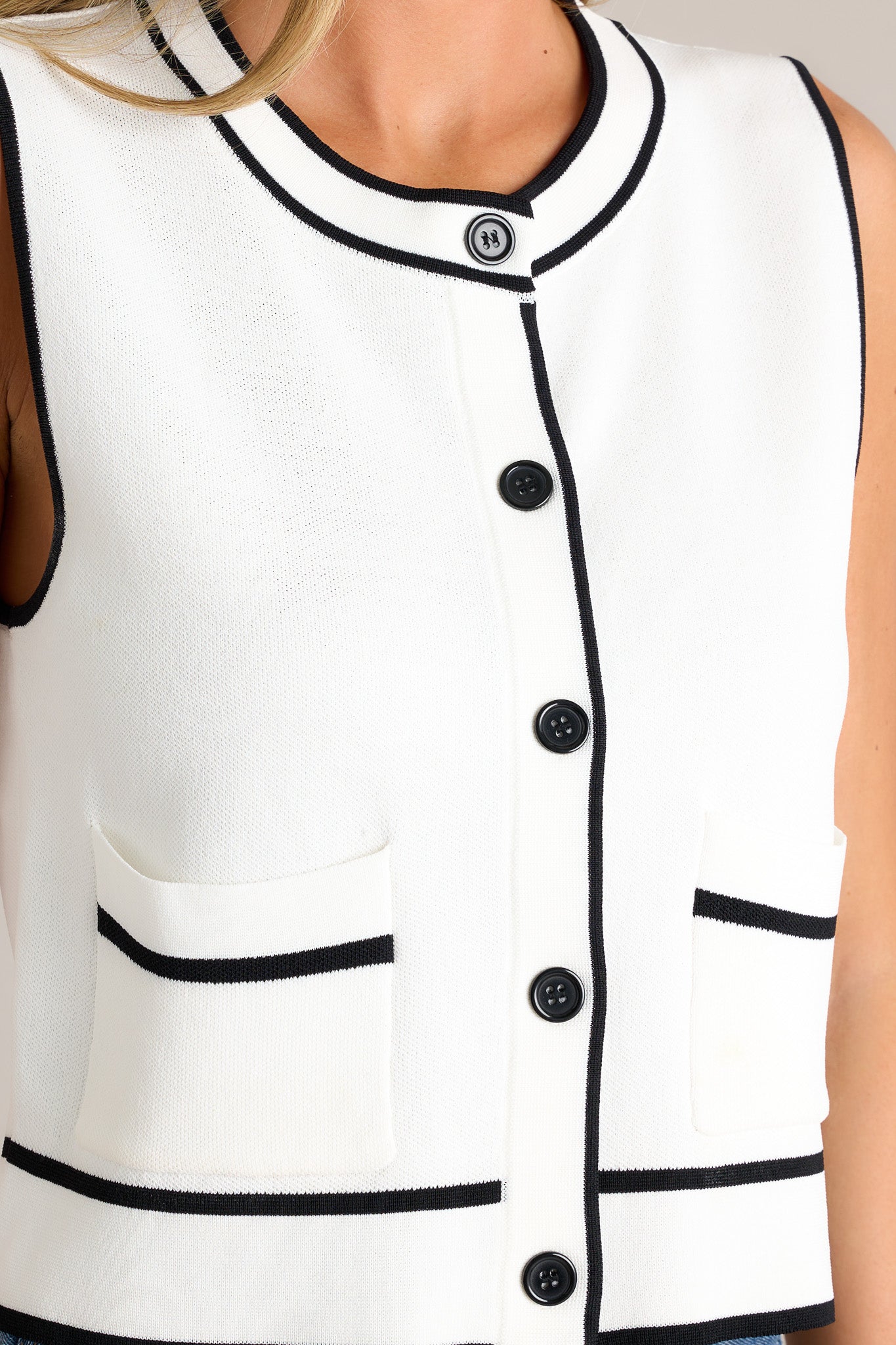 Close-up of the ivory vest showing the crew neckline, functional button front, functional pockets, and high contrasting trim.