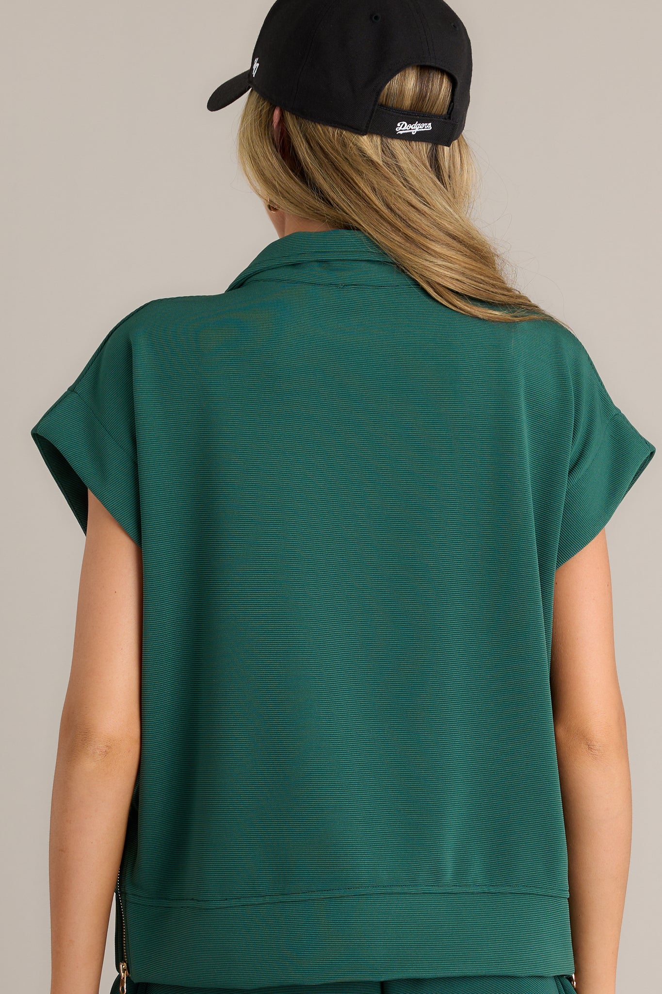 Back view of a green pullover highlighting the overall fit, short cap sleeves, and functional zippers on the sides.