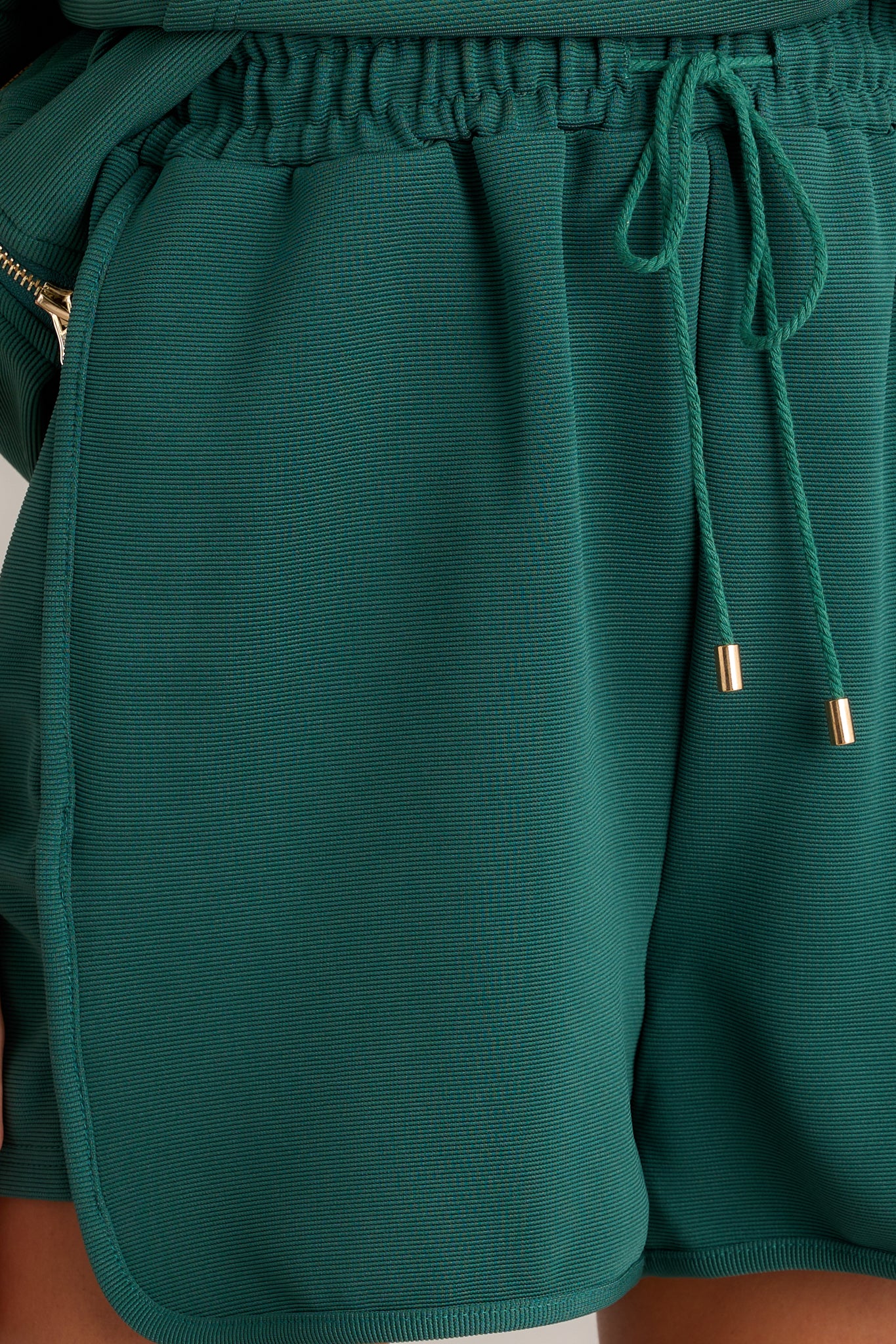 Close-up of the green shorts showing the elastic waistband, self-tie drawstring, and functional hip pockets.