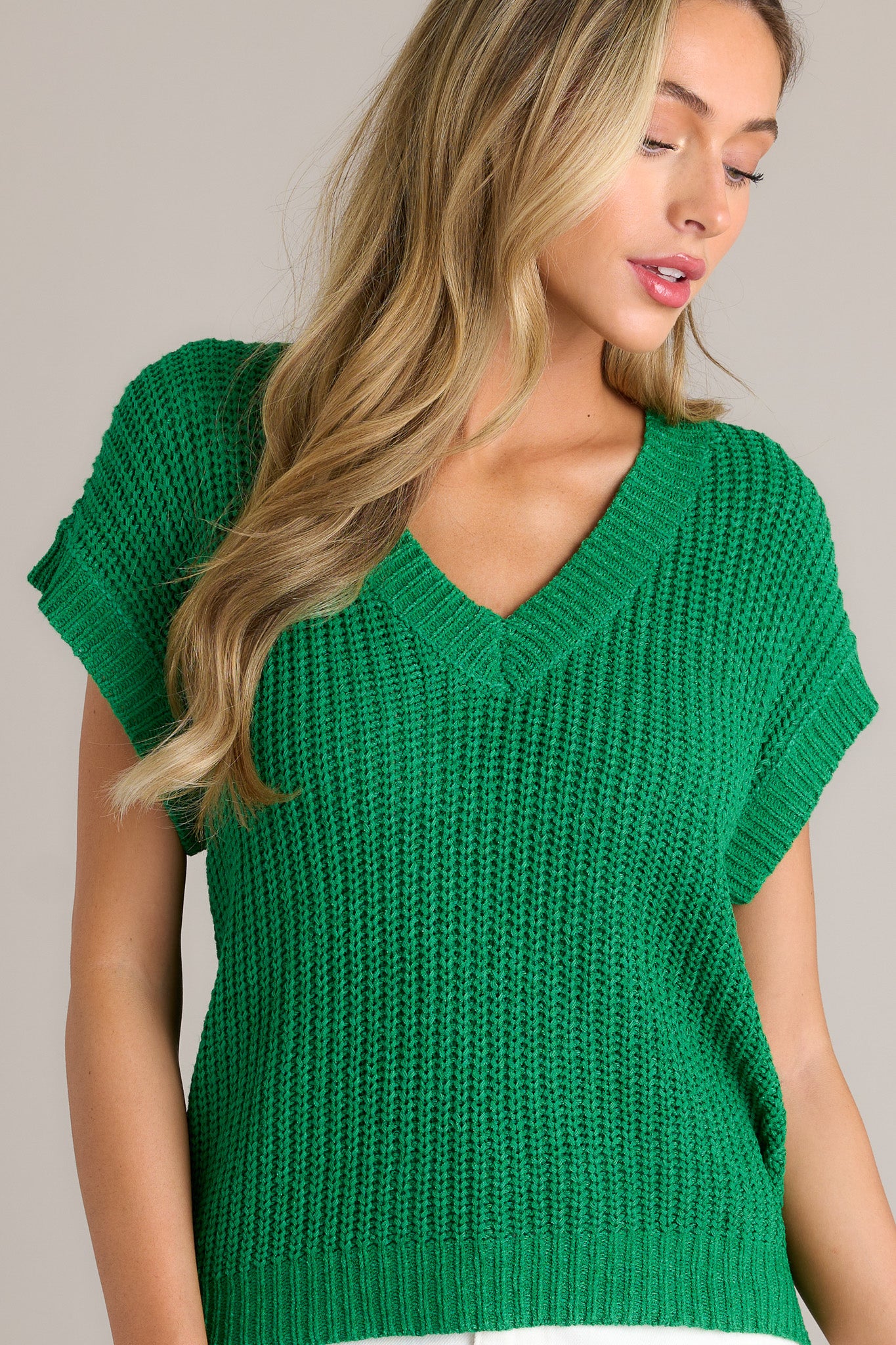 Front angled view of a kelly green sweater top featuring a ribbed v-neckline, a soft thick knit material, a ribbed hemline, and short sleeves