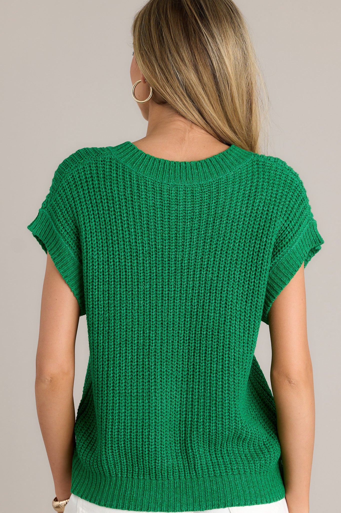 Back view of a kelly green sweater top highlighting the overall fit, ribbed hemline, and short sleeves.