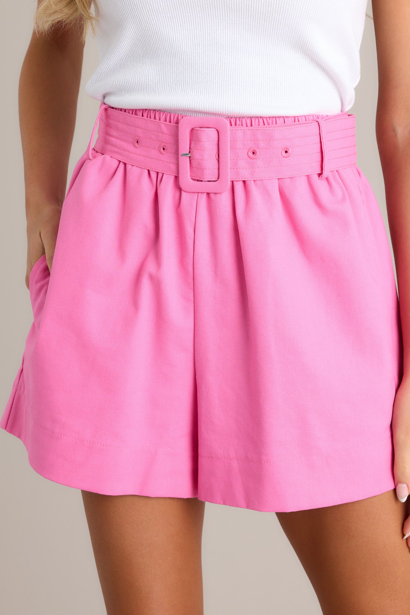 Close up view of these shorts that feature a high waisted design, an elastic waistband, a square buckle fabric belt, belt loops, and functional pockets.