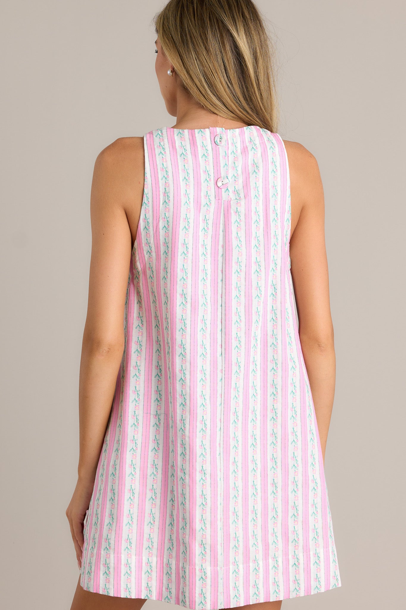 Back view of a pink floral mini dress highlighting the overall fit, thick hemline, and sleeveless design.