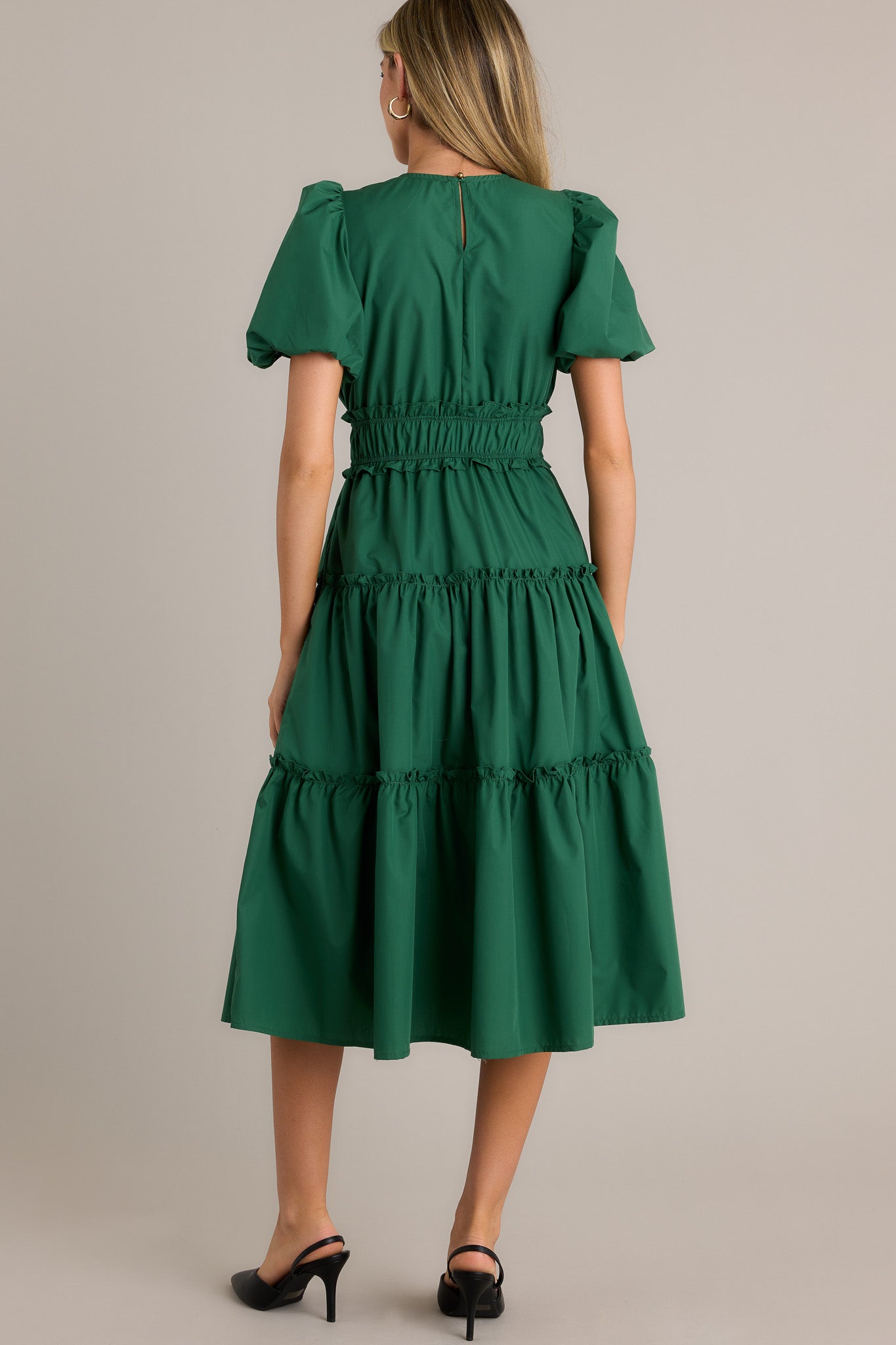 Back view of a green midi dress highlighting the overall fit, ruffled elastic waistband, and short puffed sleeves.