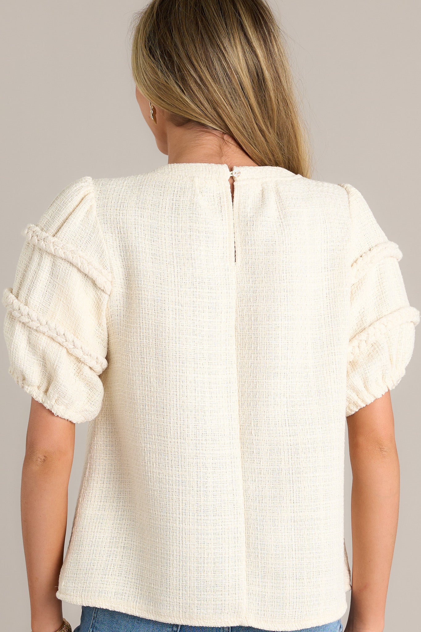 Back view of an ivory top highlighting the overall fit, tweed material, and braided detailing on the sleeves