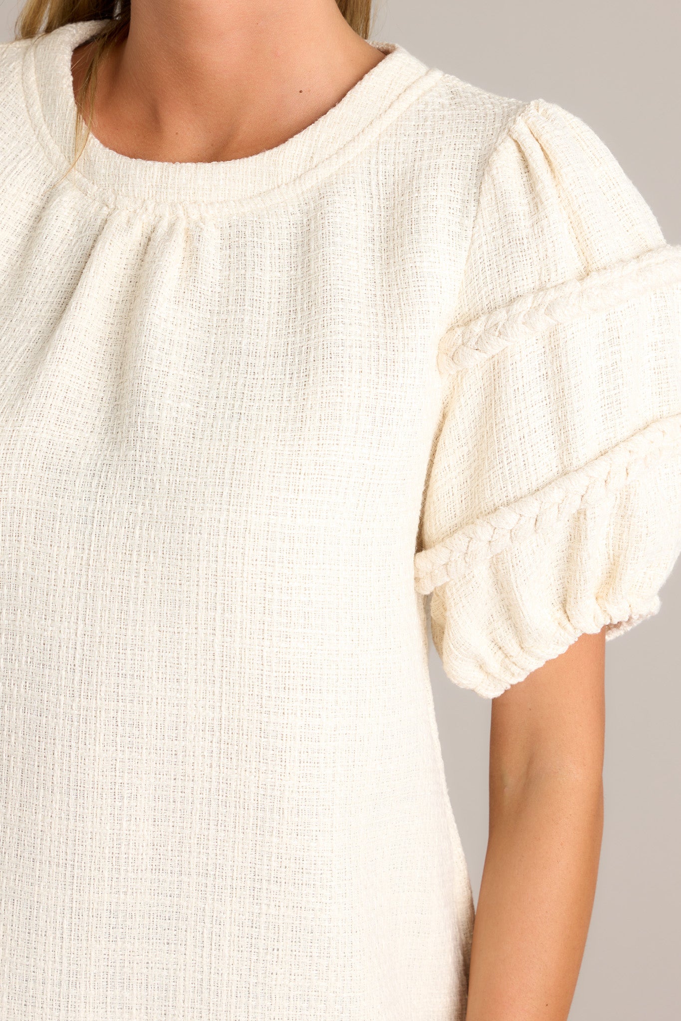 Close-up of the ivory top showing the rounded neckline, tweed material, and braided detailing on the elastic cuffed half sleeves.