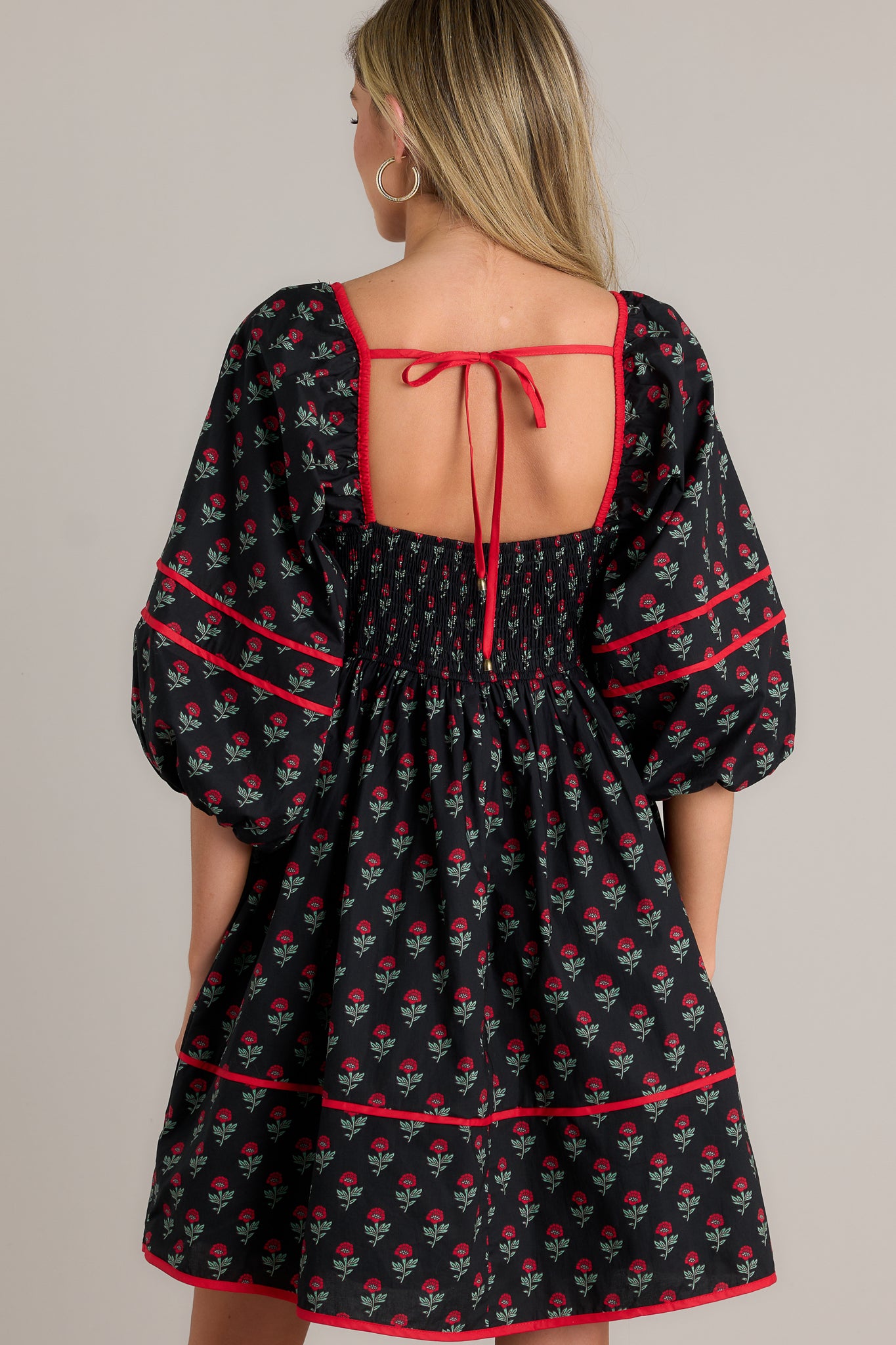 Back view of a floral puff sleeve dress highlighting the self-tie back, smocked back, and overall tiered design.