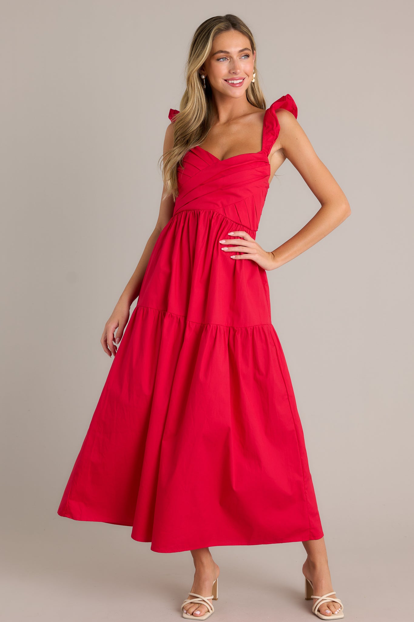 Full length view of a red midi dress with a v-neckline, a pleated bodice, a fully smocked back, a tiered design, layered flutter sleeves, and a flowing silhouette