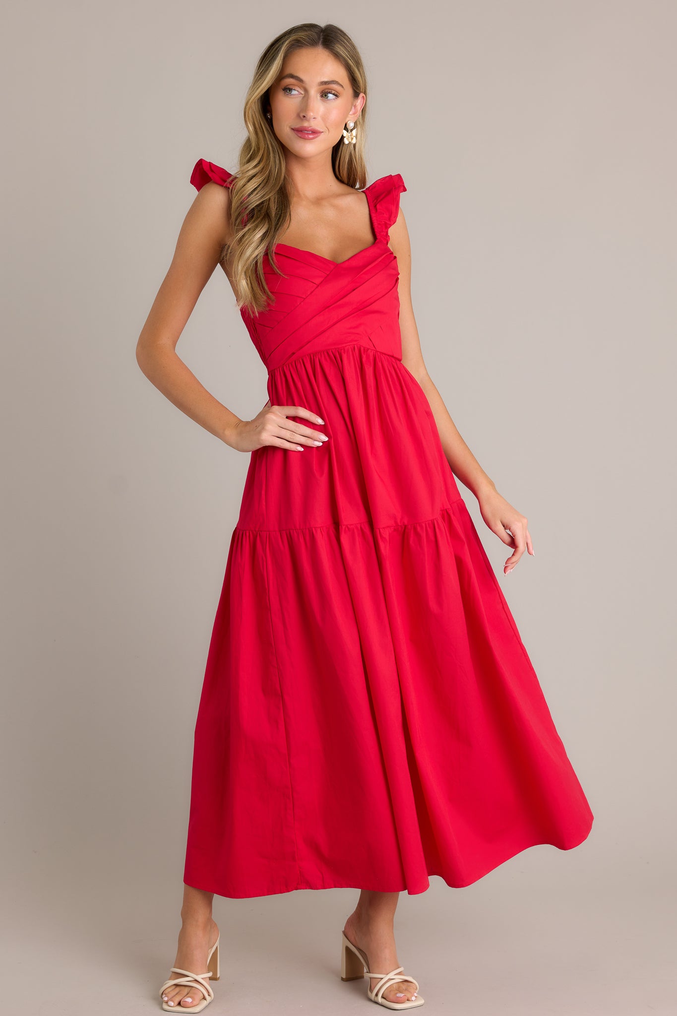 This red midi dress features a v-neckline, a pleated bodice, a fully smocked back, a tiered design, layered flutter sleeves, and a flowing silhouette.